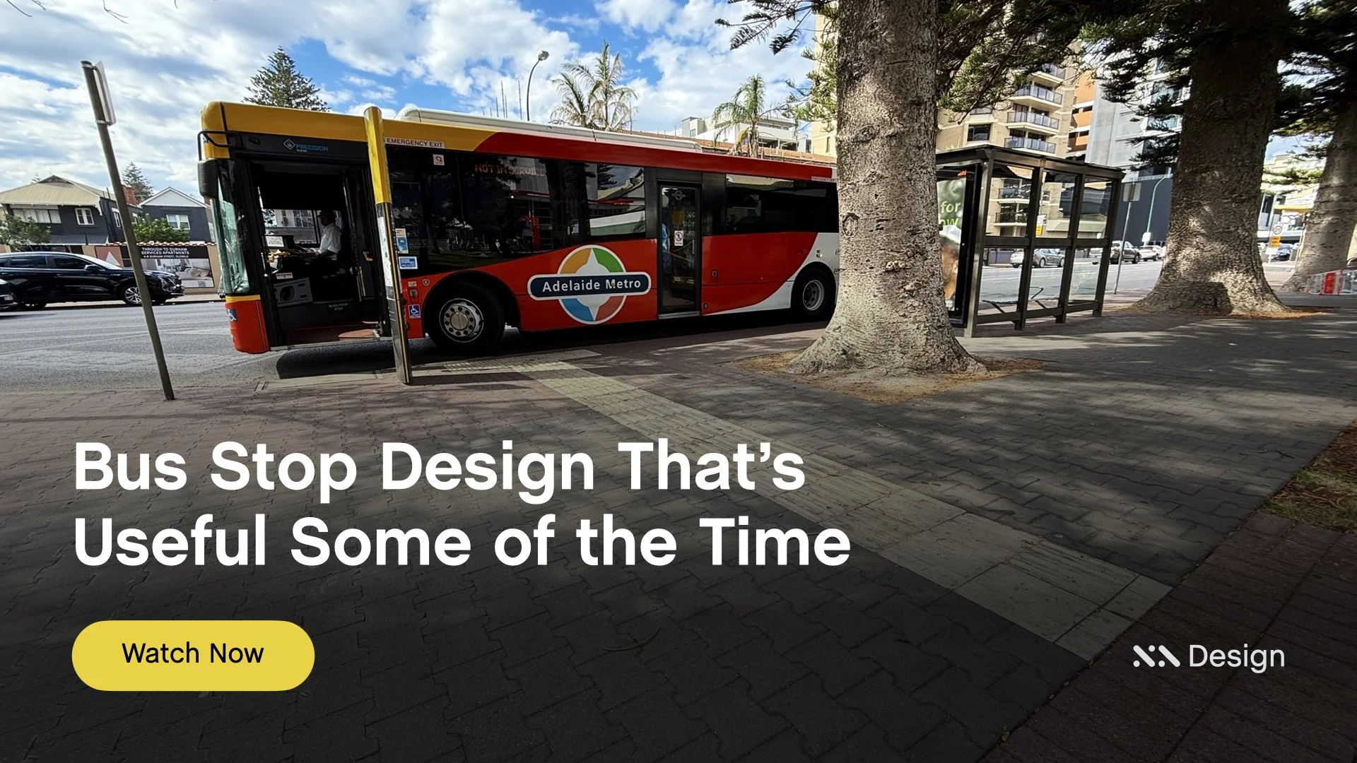 Staebl Academy - Banner for Learning Session - A red bus with Adelaide Metro logo parked at a bus stop with Tactiles (TGSIs_ on a city street, with trees and buildings in the background under a partly cloudy sky.