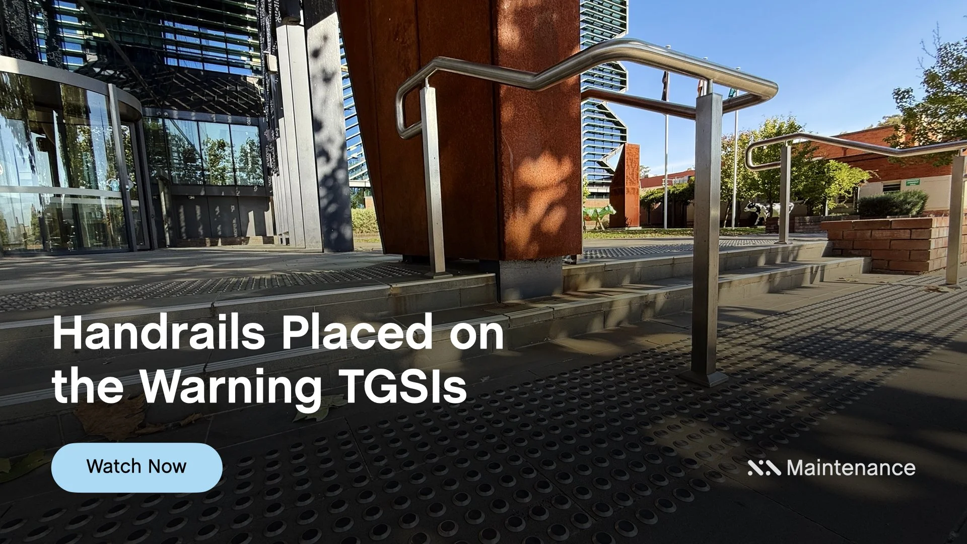 Staebl Academy - Banner for Learning Session - Steel handrails installed on top of the Warning TGSIs outside the main entrance to a modern glass building, with trees and a blue sky in the background.