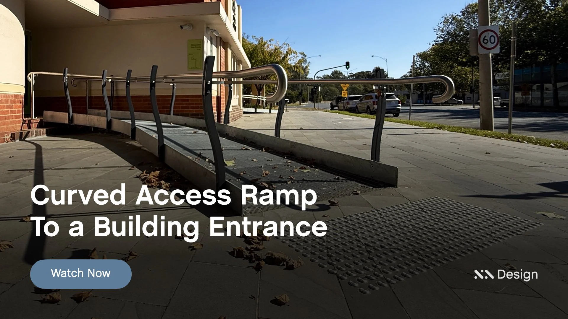 Staebl Academy - Banner for Learning Session - Curved access ramp with Tactiles (TGSIs) leading to a building entrance with a metal handrail and surrounding sidewalk with fallen leaves, adjacent to a street with cars and a speed limit sign.