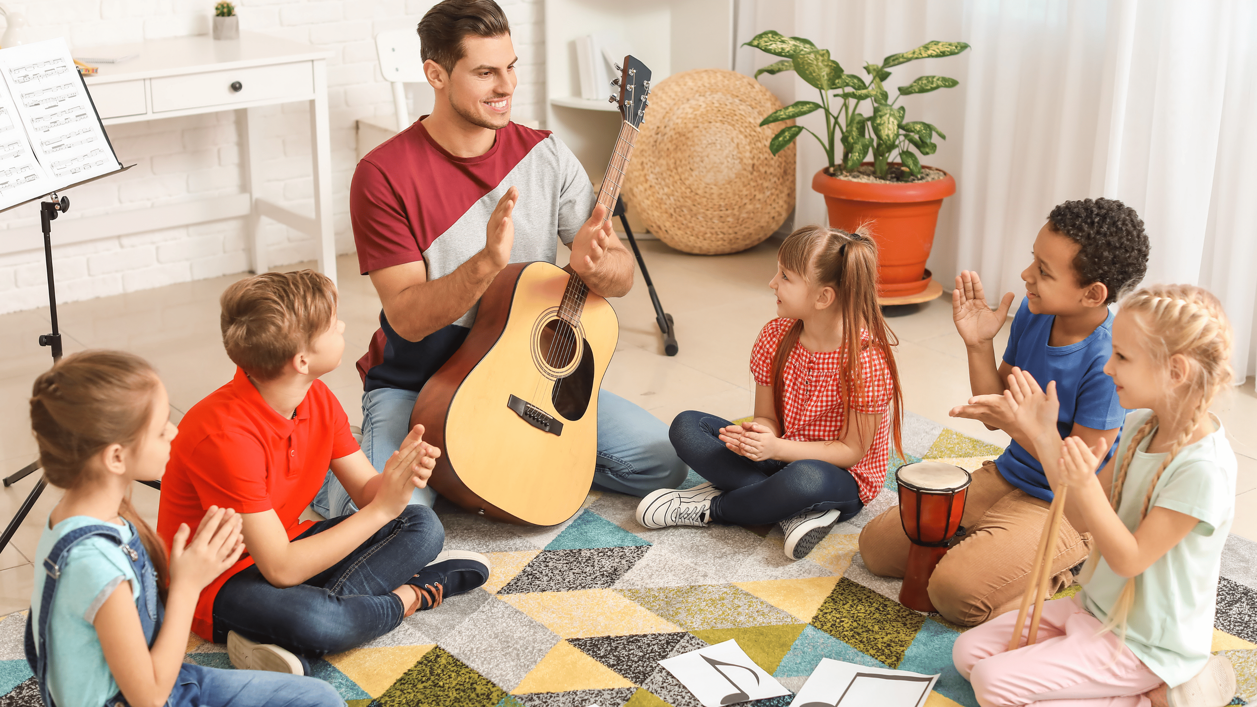 Music teacher clapping while sitting with children in a circle, playing guitar and practicing rhythm together.