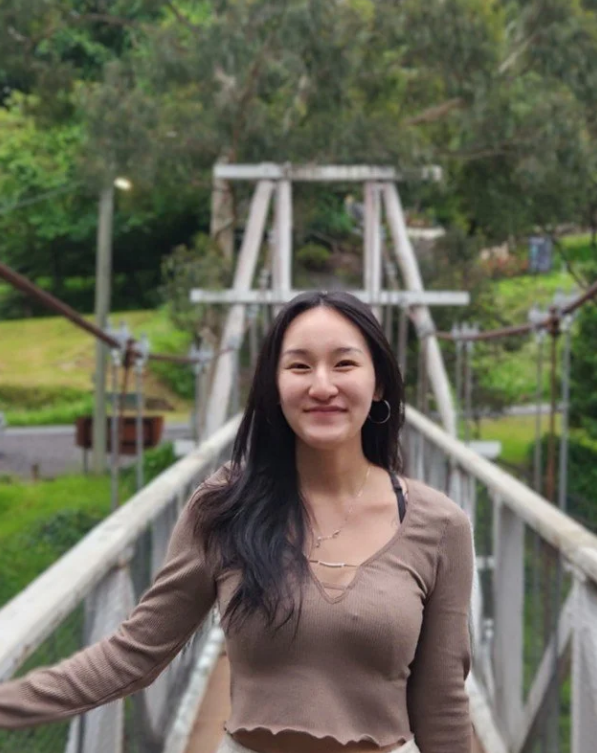 Person smiling while standing on a narrow suspension bridge surrounded by lush greenery.