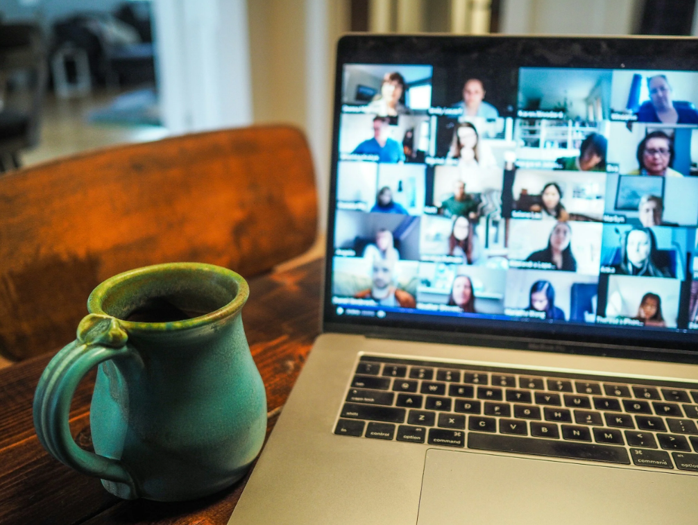 Teal ceramic mug next to a laptop showing a multi-person video call on a wooden table.