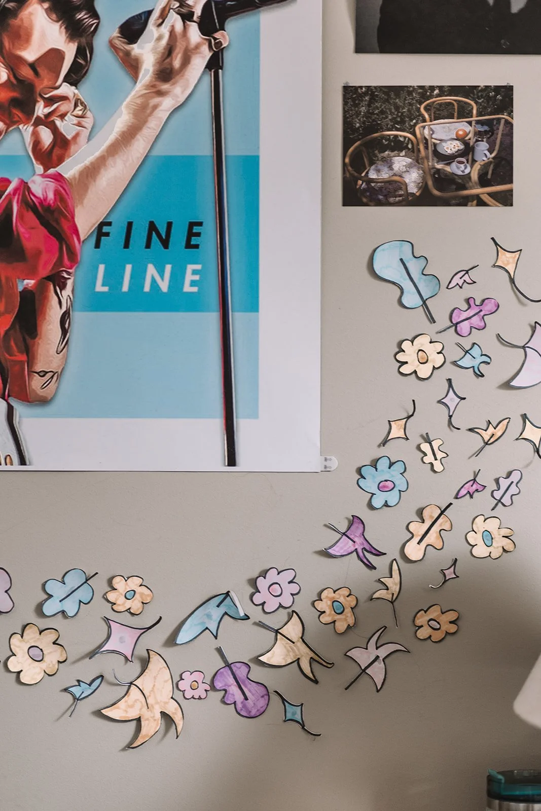 Wall with a “Fine Line” poster, small photos, and colorful paper flower and bird cutouts arranged decoratively