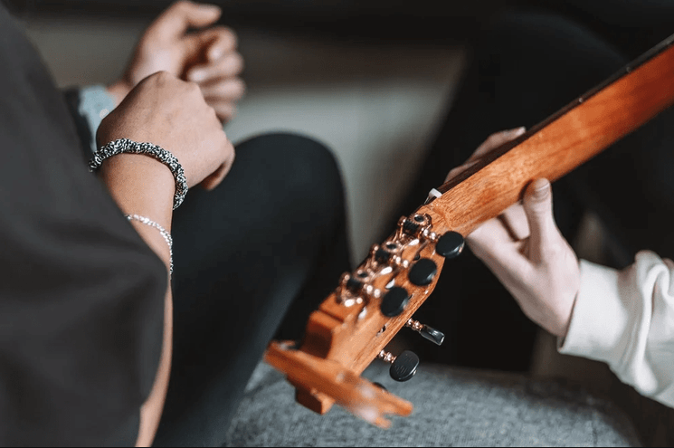 Close-up of a guitar headstock as a child holds it while an adult gestures nearby during a lesson.