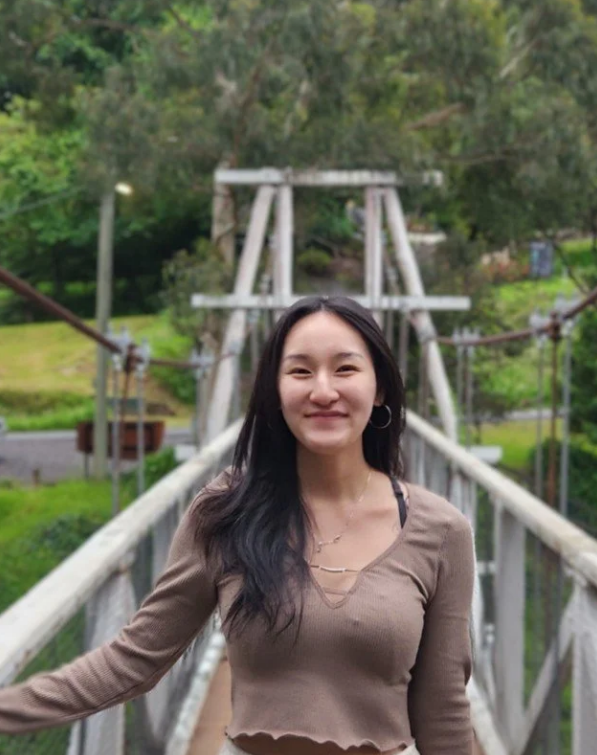 Person smiling while standing on a narrow suspension bridge surrounded by lush greenery.