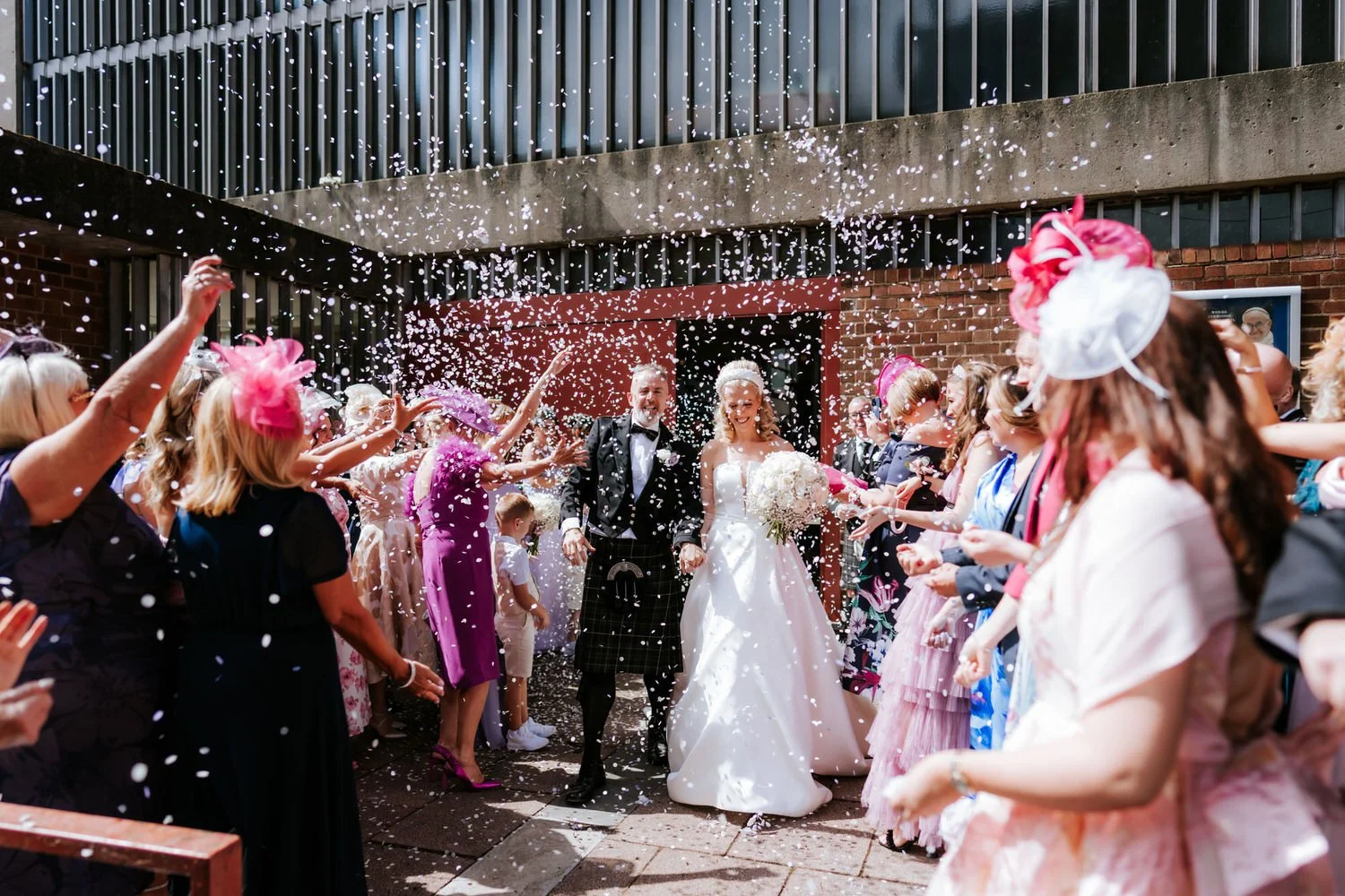 Bride and groom walking outside surrounded by friends and family throwing confetti at their wedding celebration.