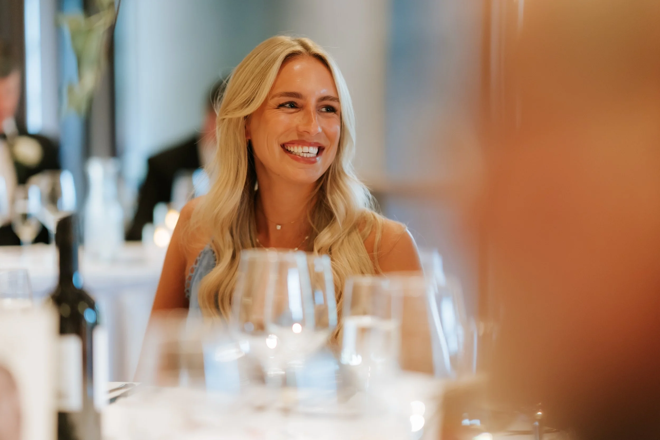 A candid portrait of a smiling guest framed by reception glassware.