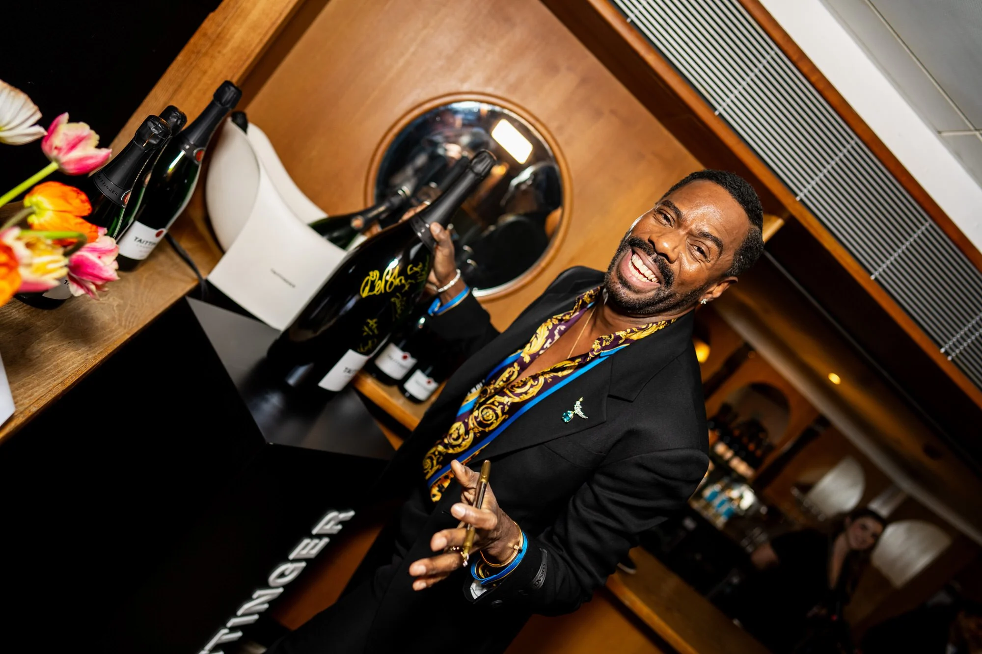 Colman Domingo laughing while signing a champagne bottle backstage at the BAFTAs.