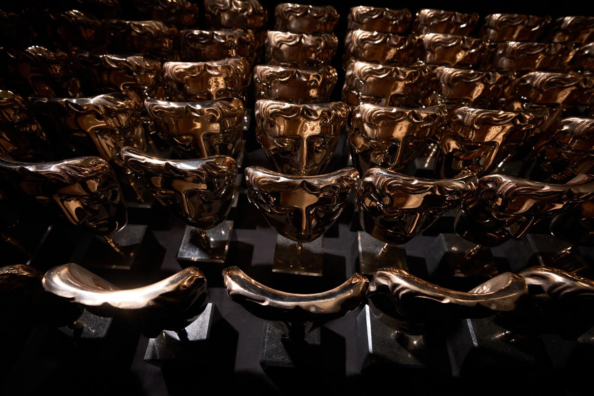 Multiple shiny, metallic, gold-colored awards shaped like abstract human faces arranged in rows.