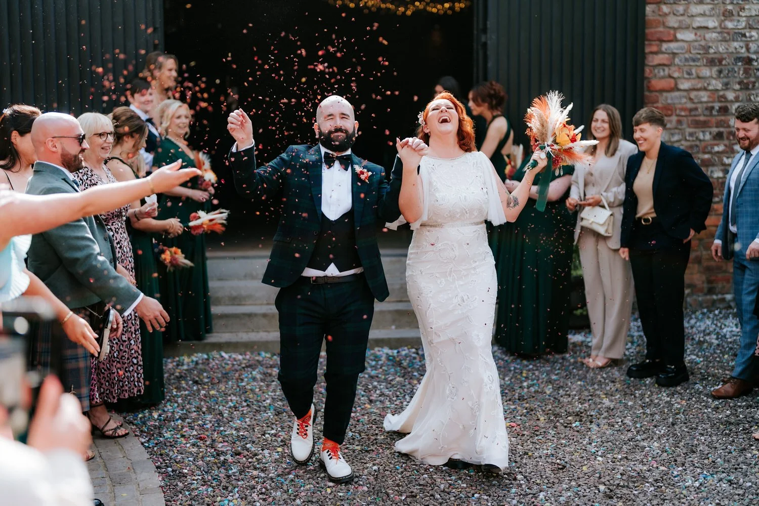 A newly married couple celebrates with friends and family with confetti at an outdoor wedding reception.