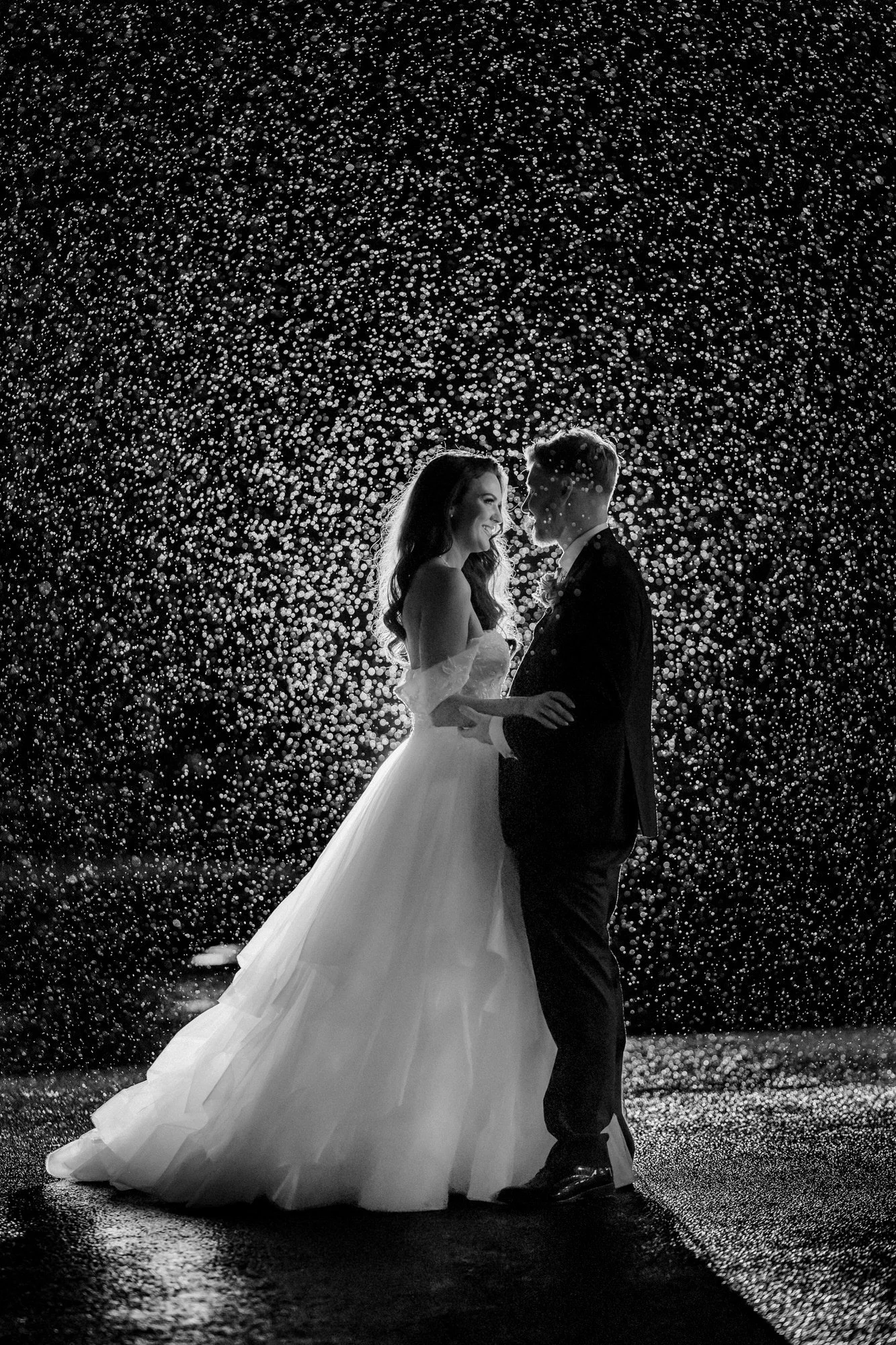 Black-and-white portrait of the bride and groom surrounded by backlit droplets at night
