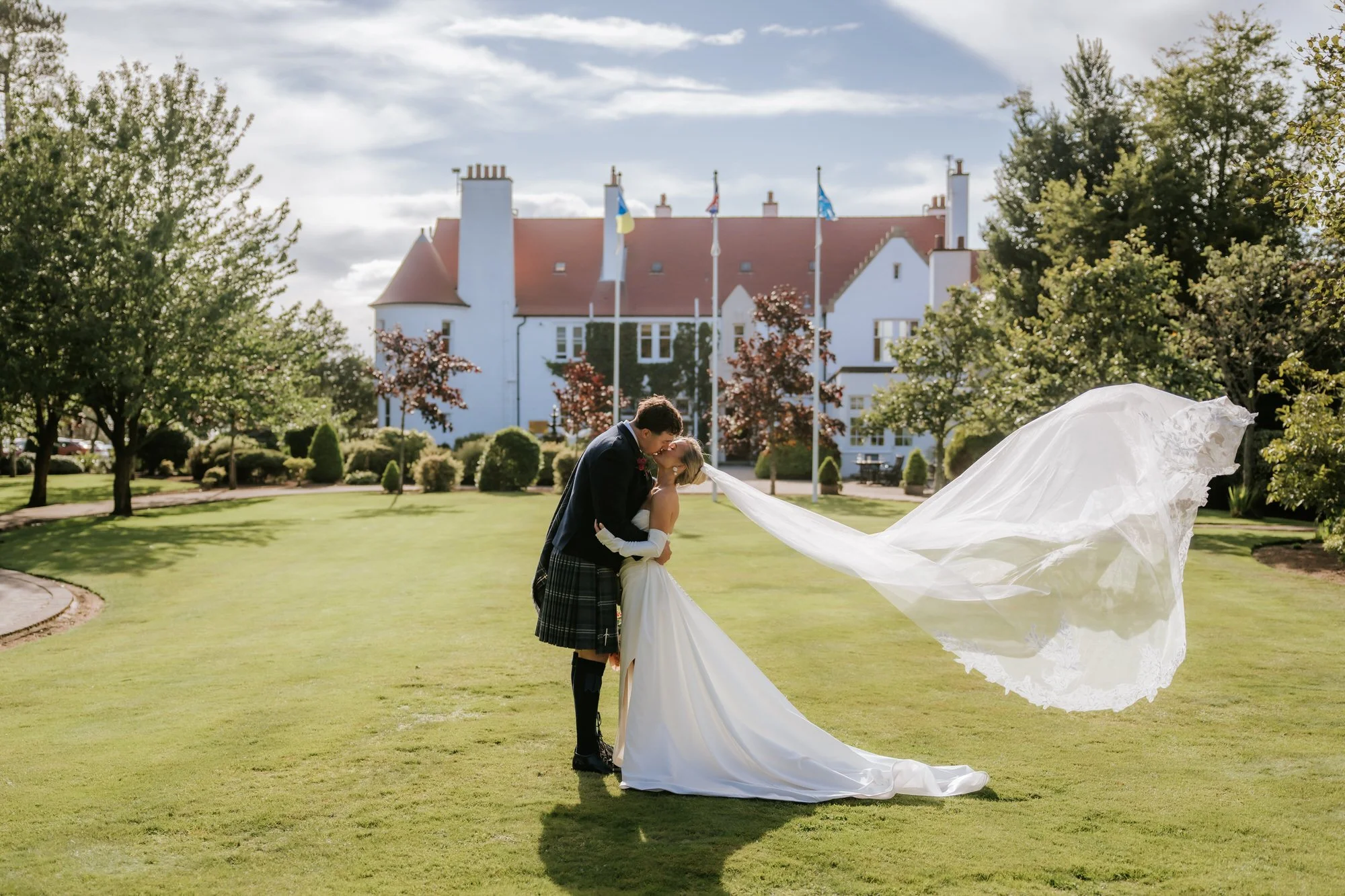 Fiona and Connor kissing outside Lochgreen with her veil blowing in the breeze.