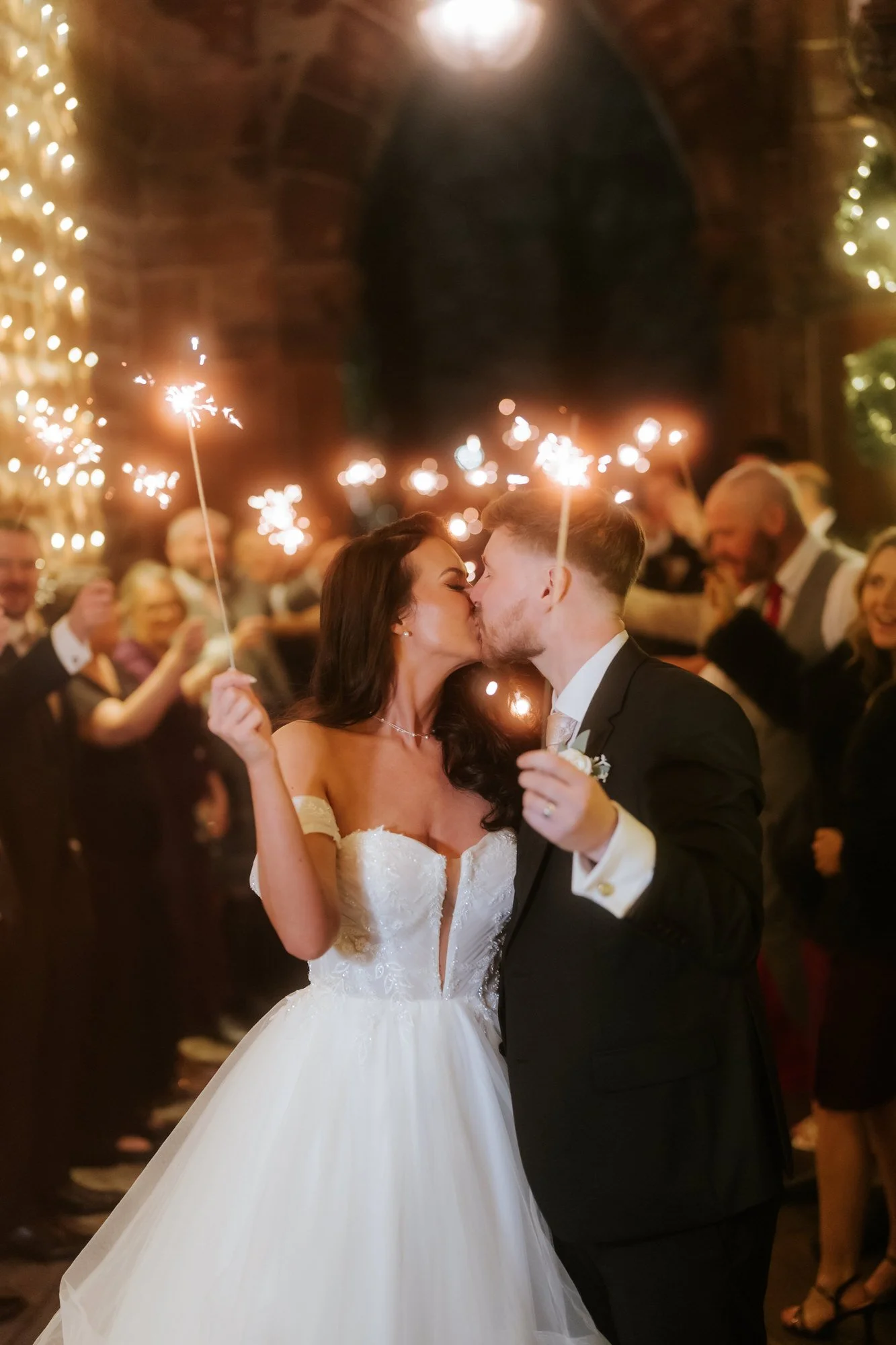 Bride and groom kissing among guests holding sparklers