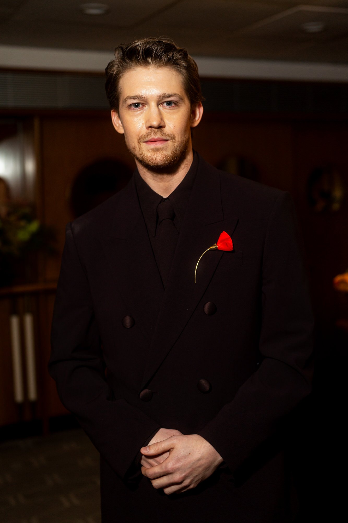 Joe Alwyn wearing a dark suit with a red rose pin at the 2025 BAFTA Film Awards.
