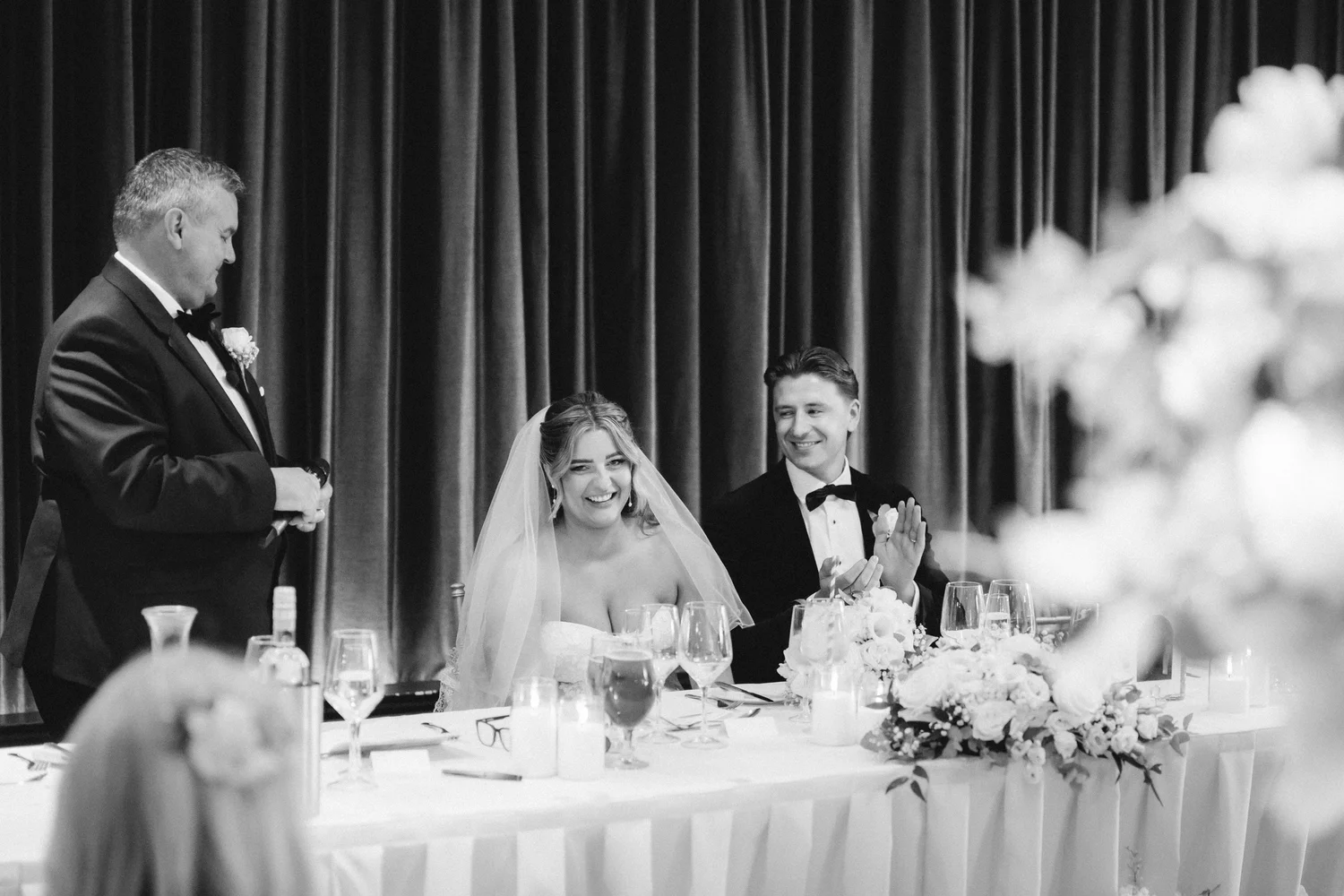 Emma and Frazer laughing at the top table as a wedding speech is delivered.