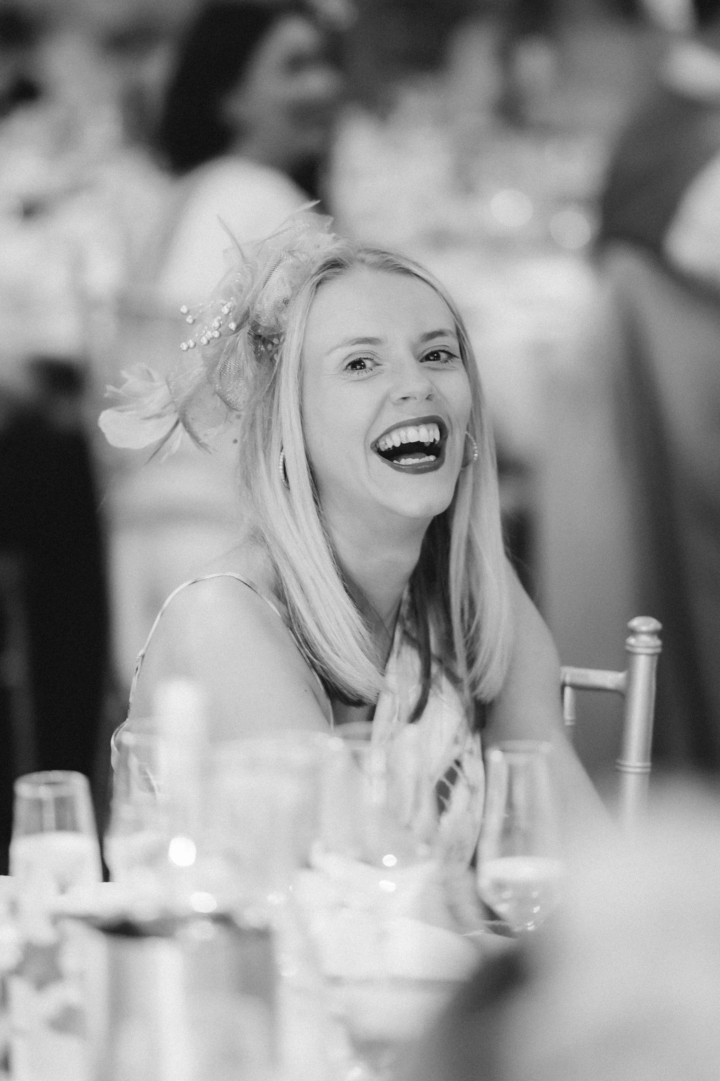 A guest laughing openly during the wedding speeches, photographed in black and white.