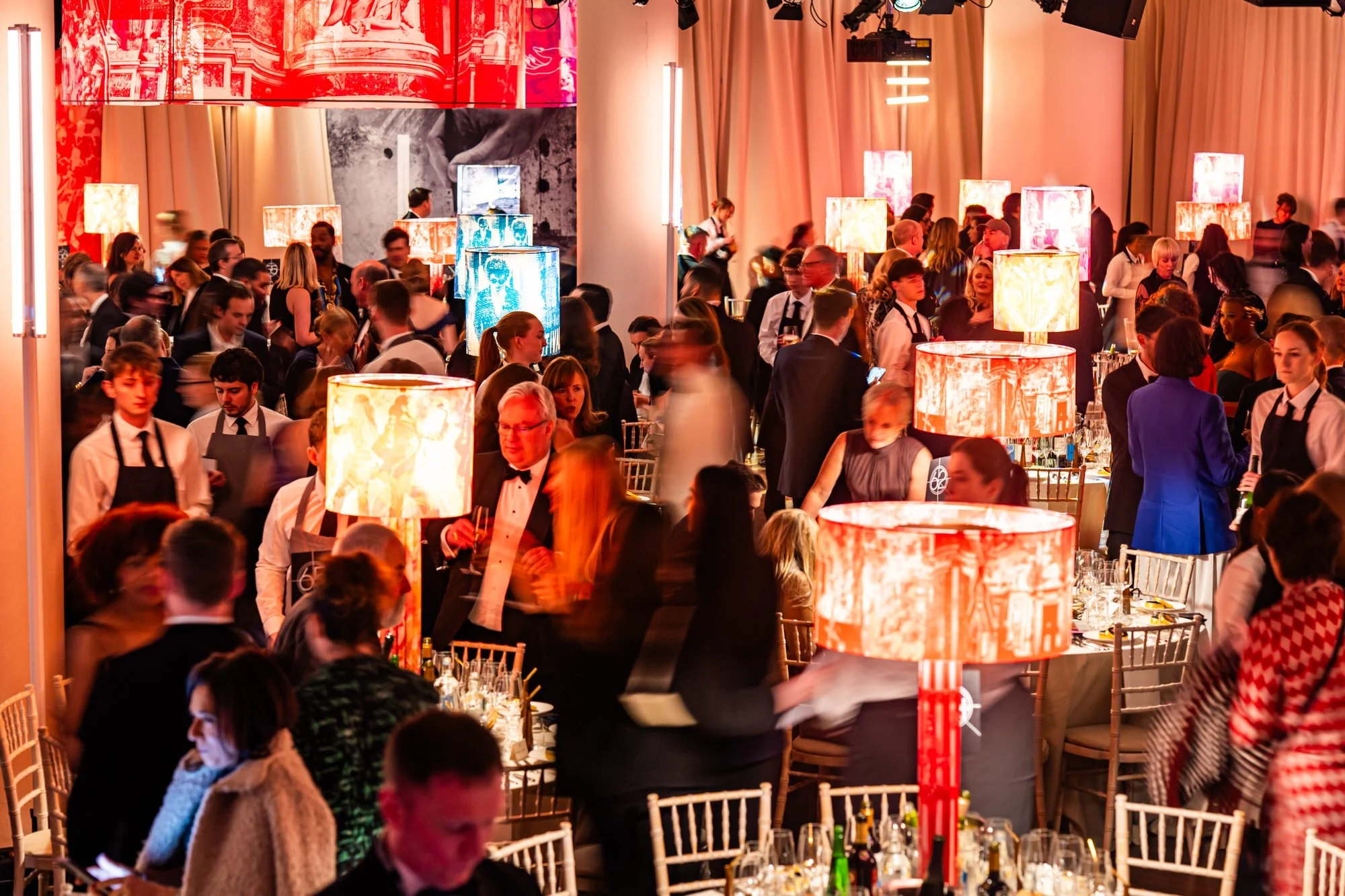 Guests and waiting staff moving through the BAFTA dinner, captured with motion blur and warm lighting.