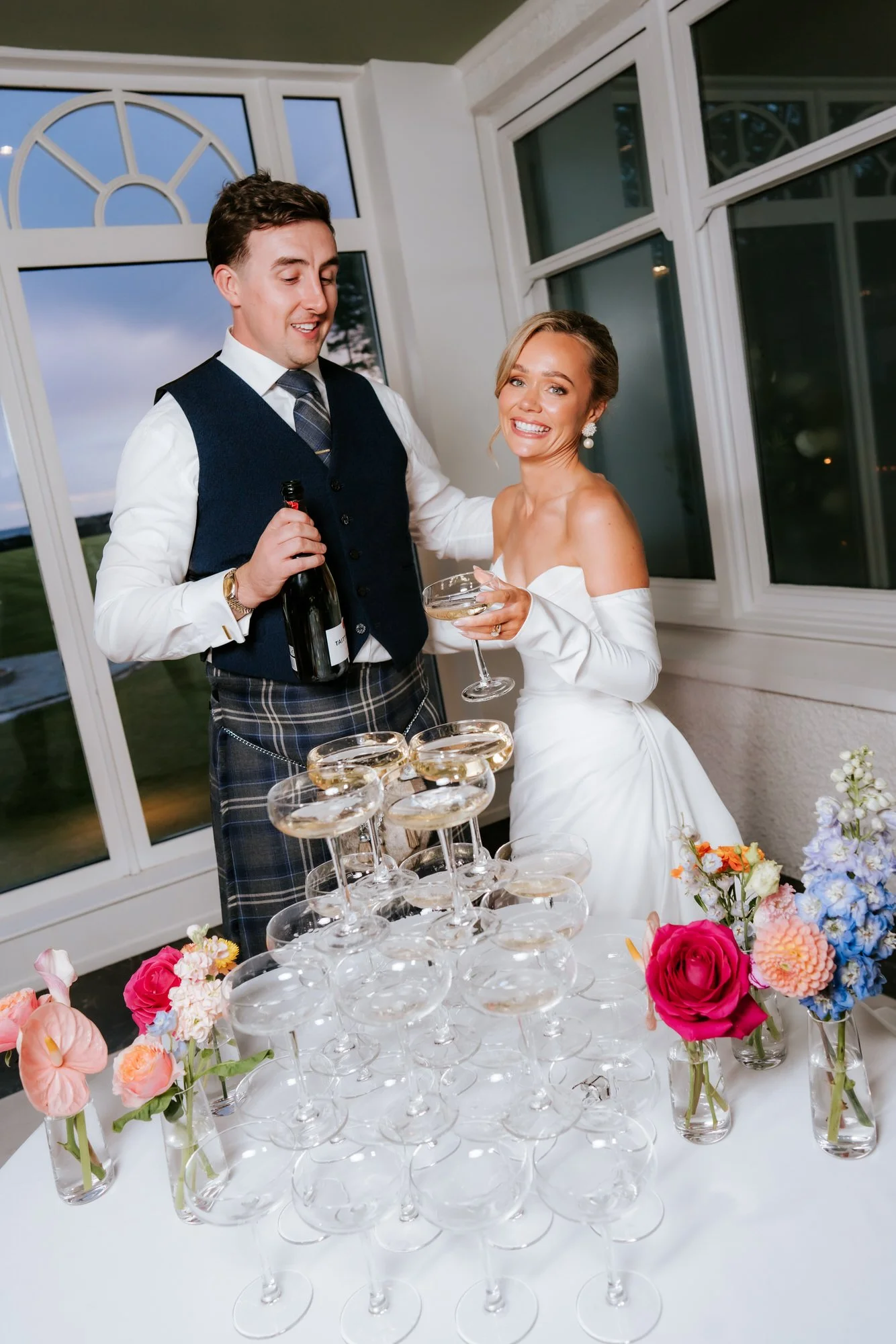 Fiona and Connor pouring champagne into a tower of glasses.