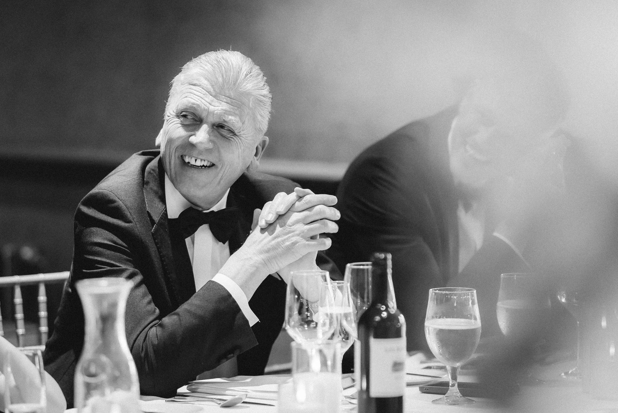 A guest smiling with hands clasped during the speeches.