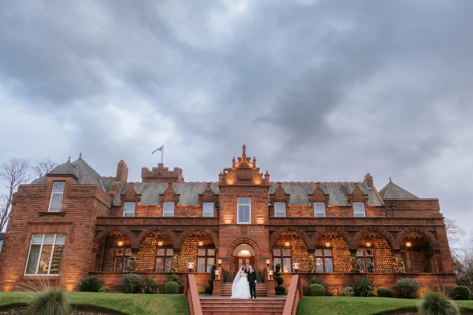 Wide view of Boclair House at dusk with the couple on the front steps