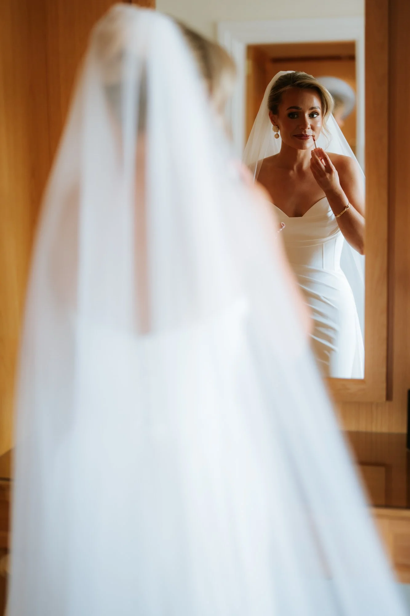 Fiona applying lipstick in the mirror during bridal preparations.