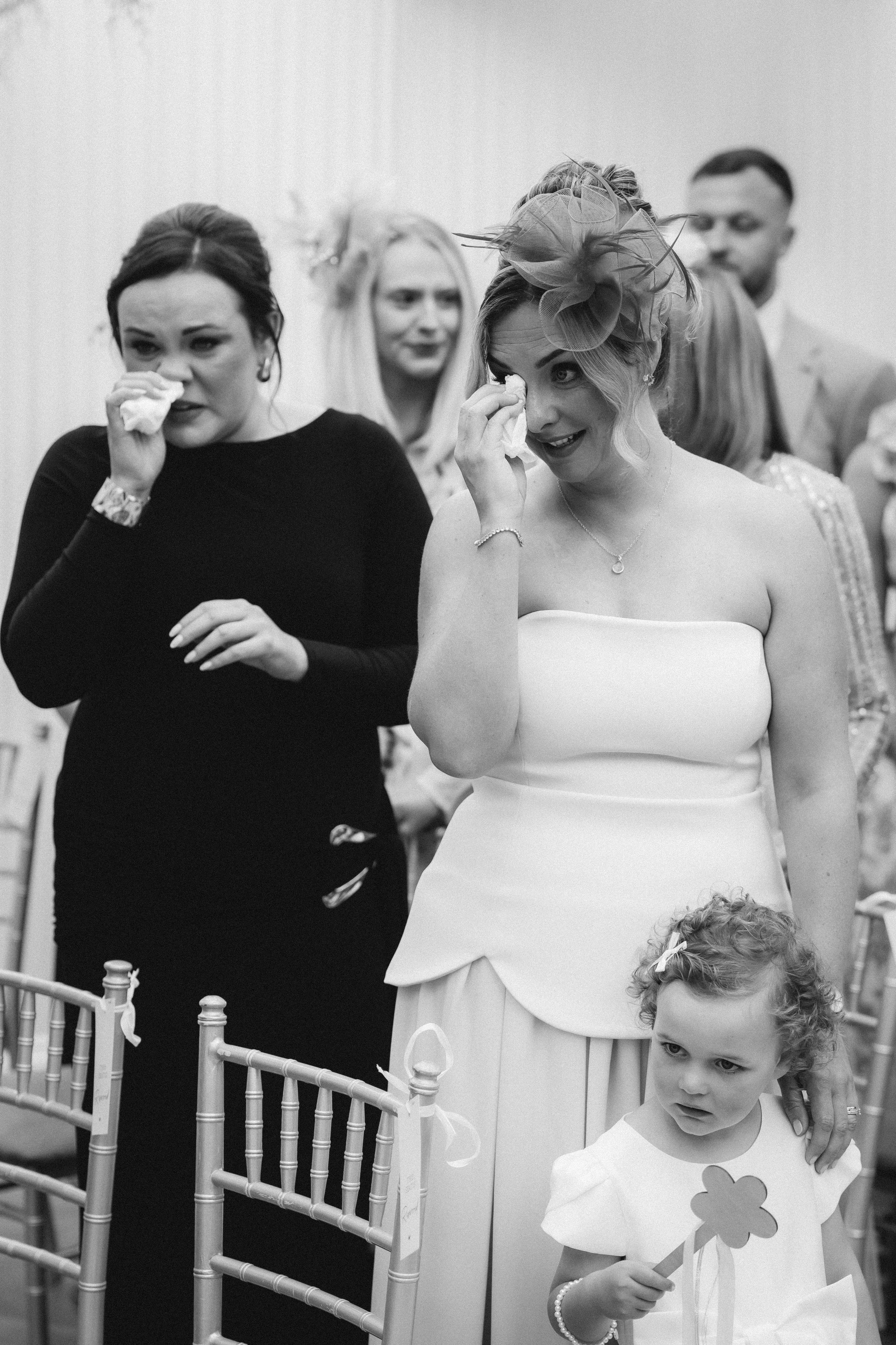 Emma and wedding guests during the ceremony, photographed in black and white.
