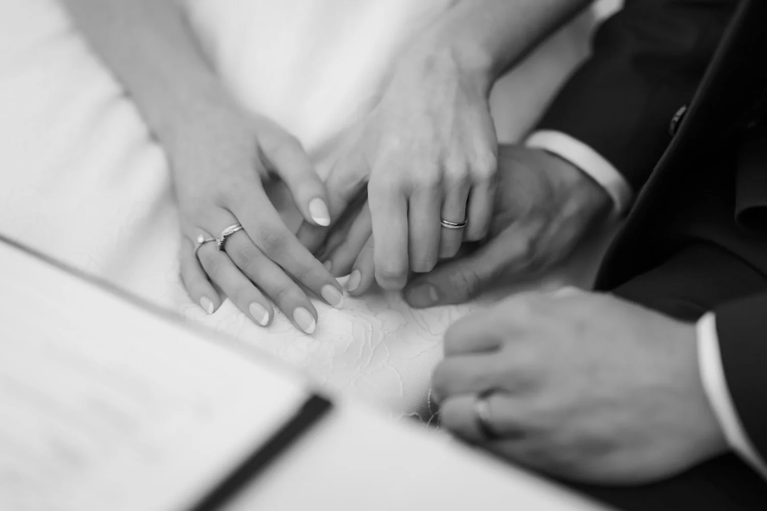 Close-up of a wedding ceremony with a couple's hands and rings, with one person's hand resting on the table and the other's hand holding it.
