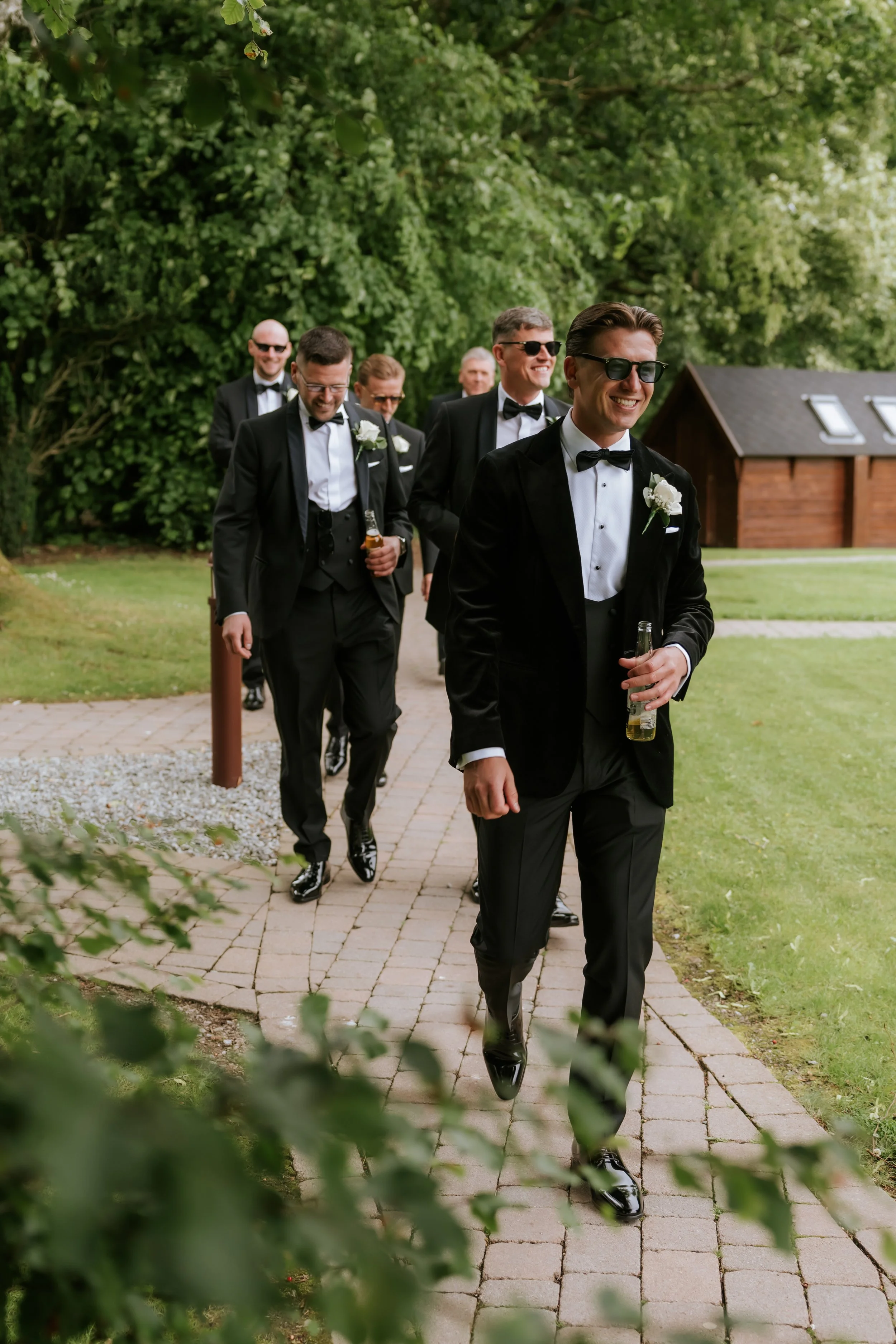 Frazer and his groomsmen walking through the castle grounds in black suits and sunglasses.