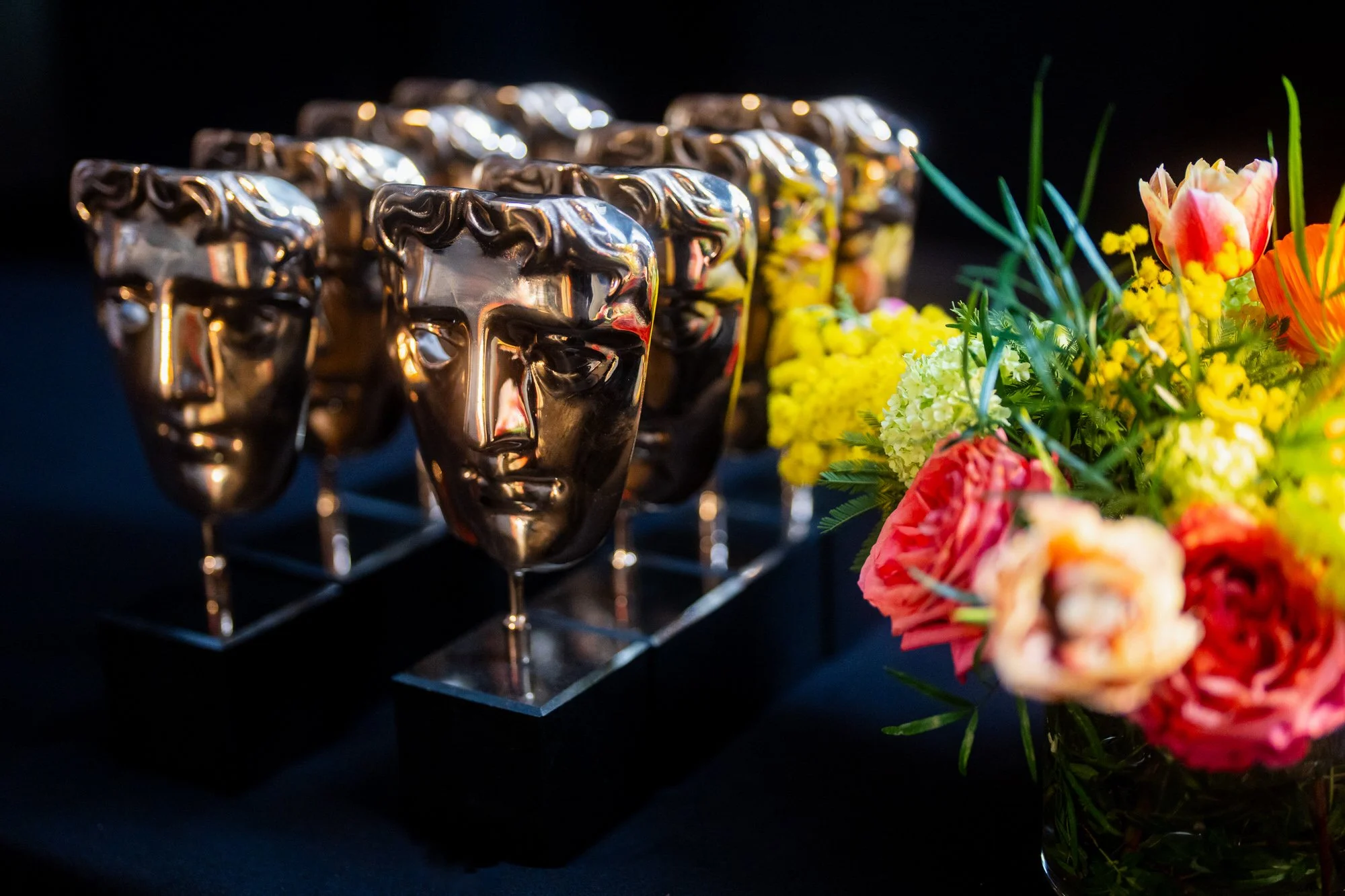 BAFTA trophies arranged beside colourful flowers on a backstage table.