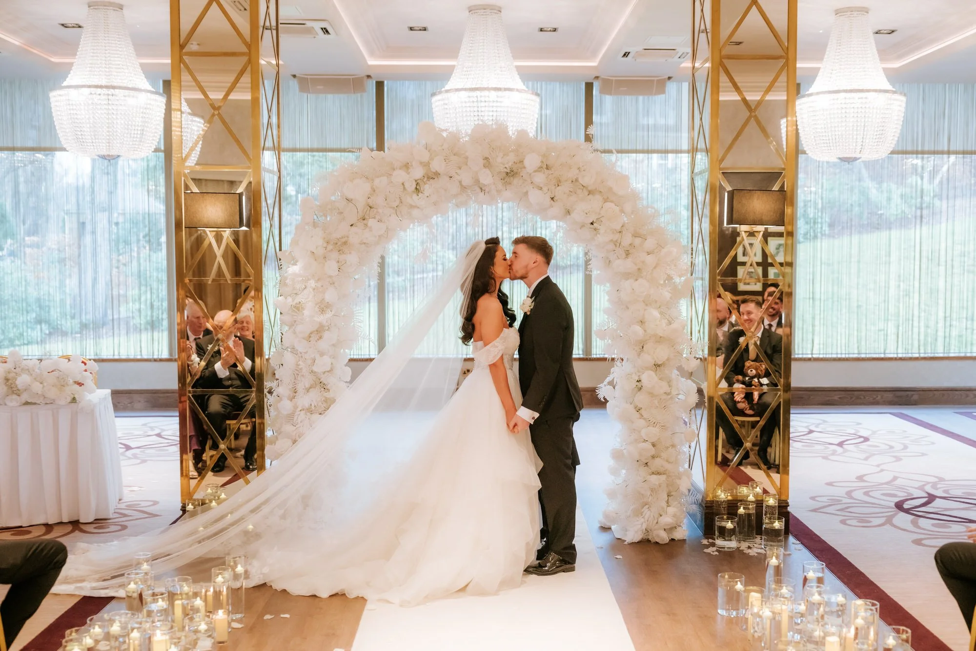 Bride and groom sharing their first kiss beneath a floral arch