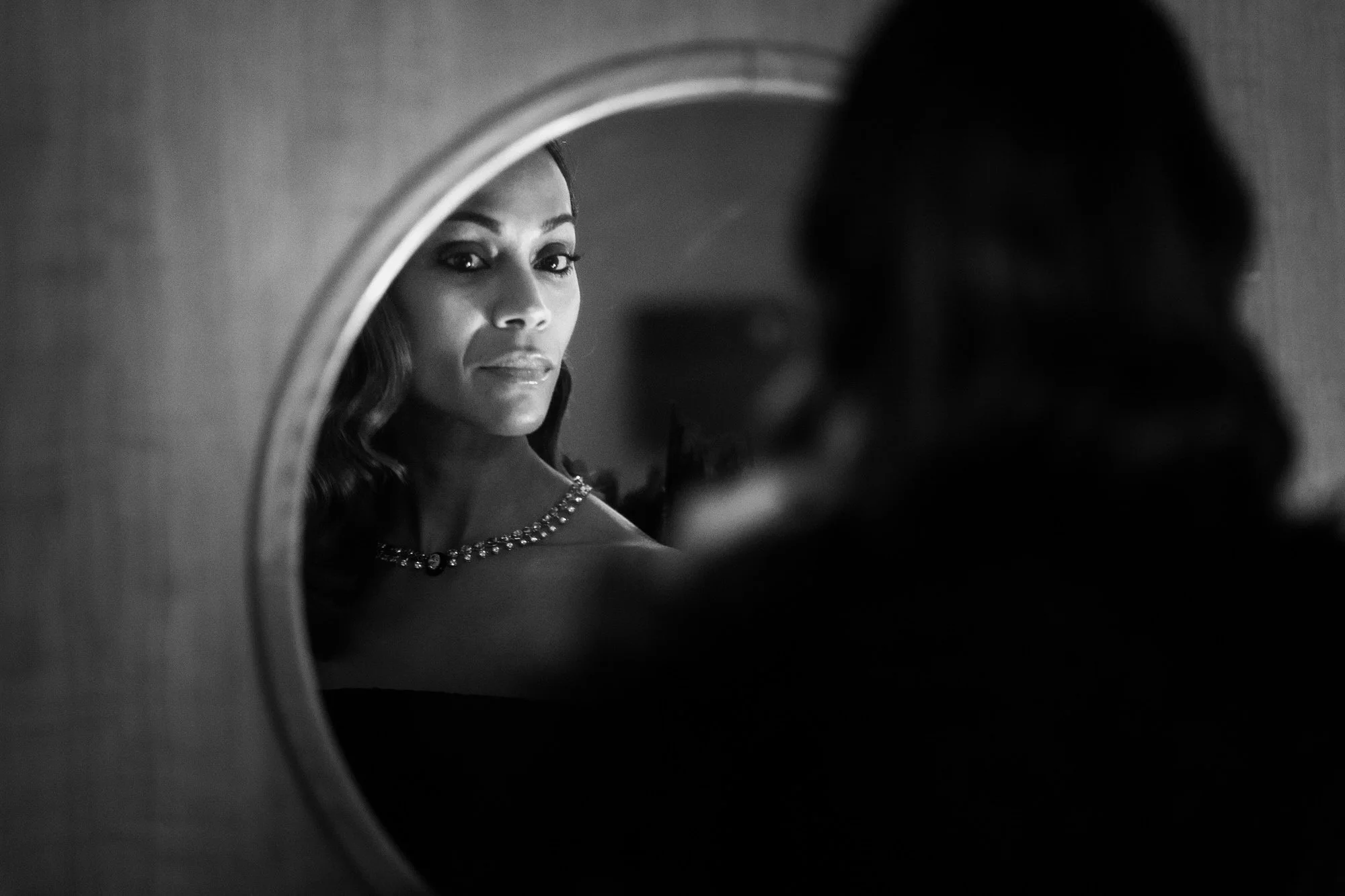 Zoë Saldaña reflected in a backstage mirror at the 2025 BAFTA Film Awards, photographed in black and white.