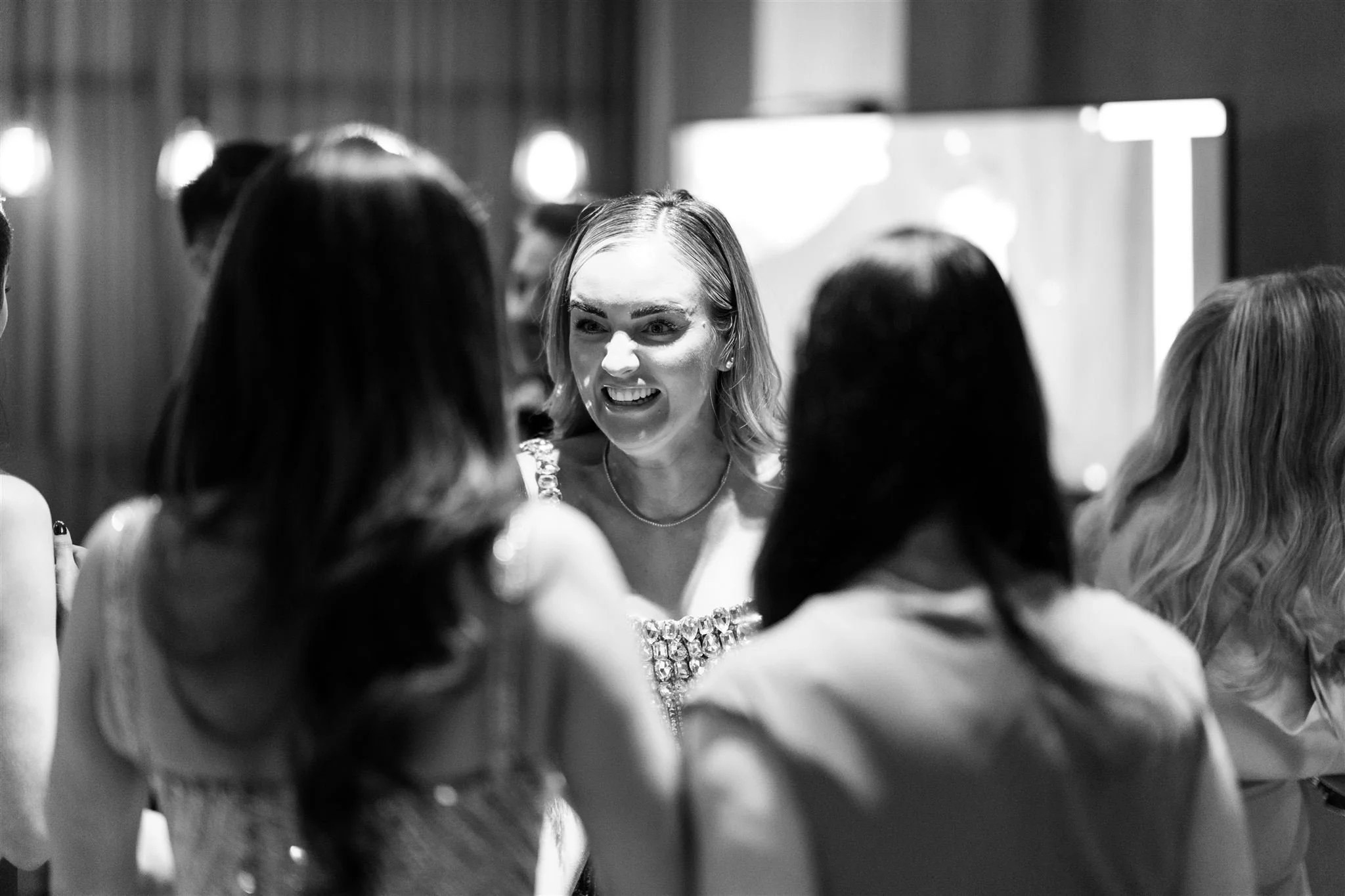 Black and white photo of a woman talking to a group of women at an indoor event