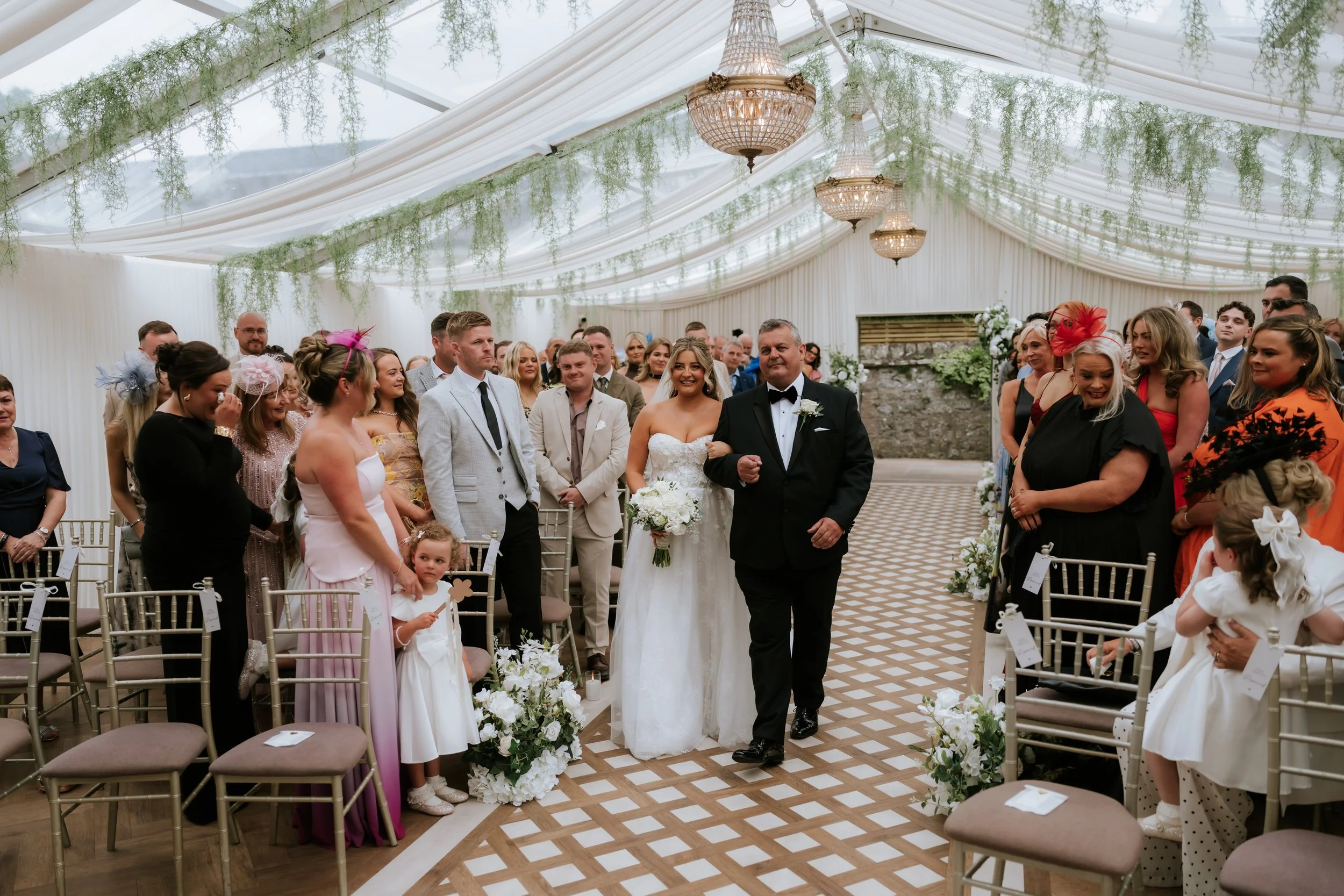 Emma arriving for the ceremony beneath the pavilion’s drapery and chandeliers.