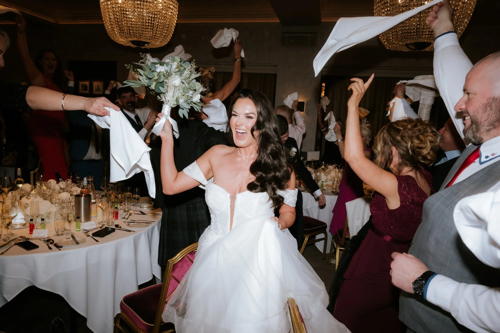 Bride raising her bouquet as guests celebrate around her
