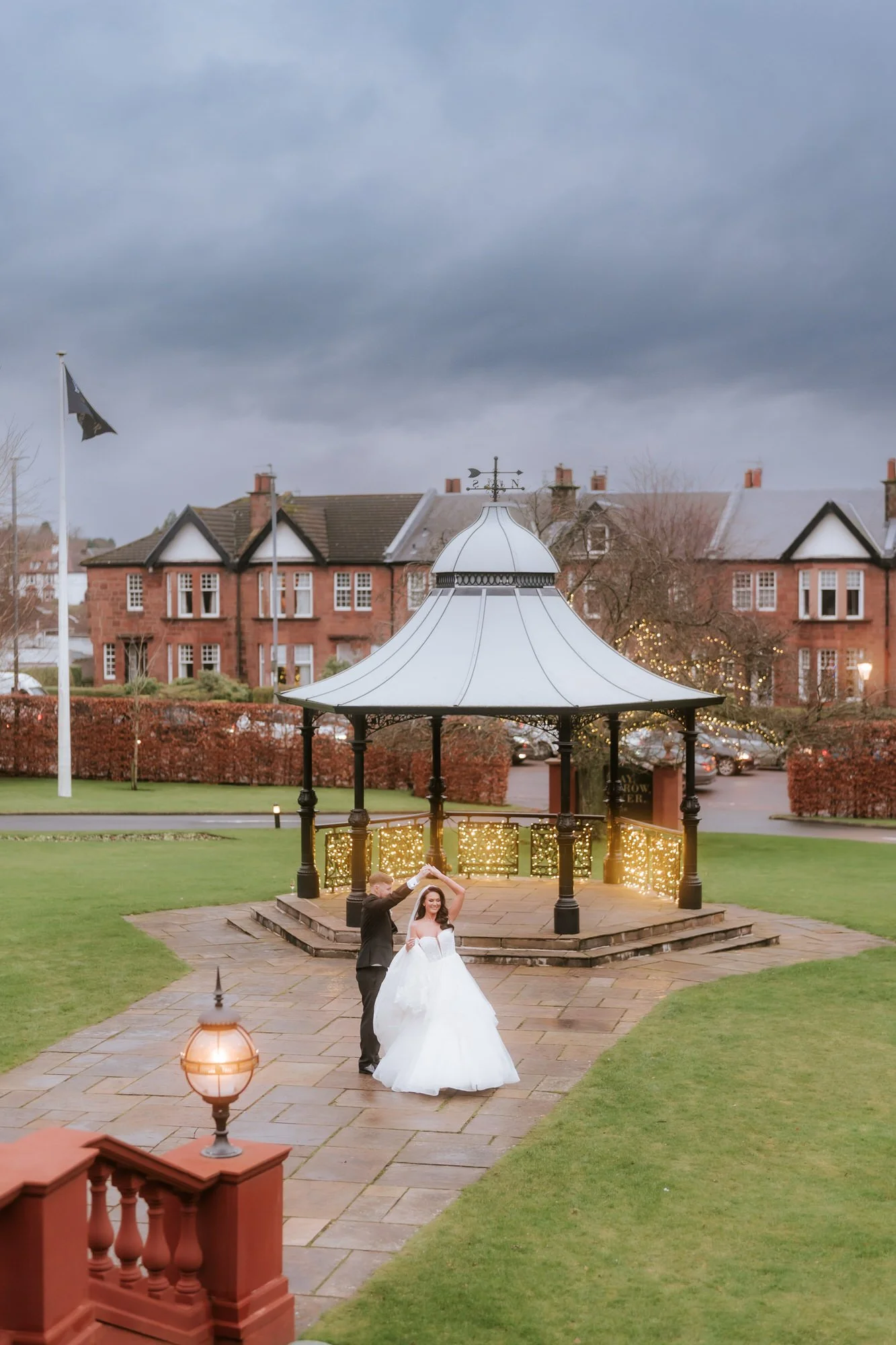 Groom twirling the bride beside the illuminated bandstand at Boclair House