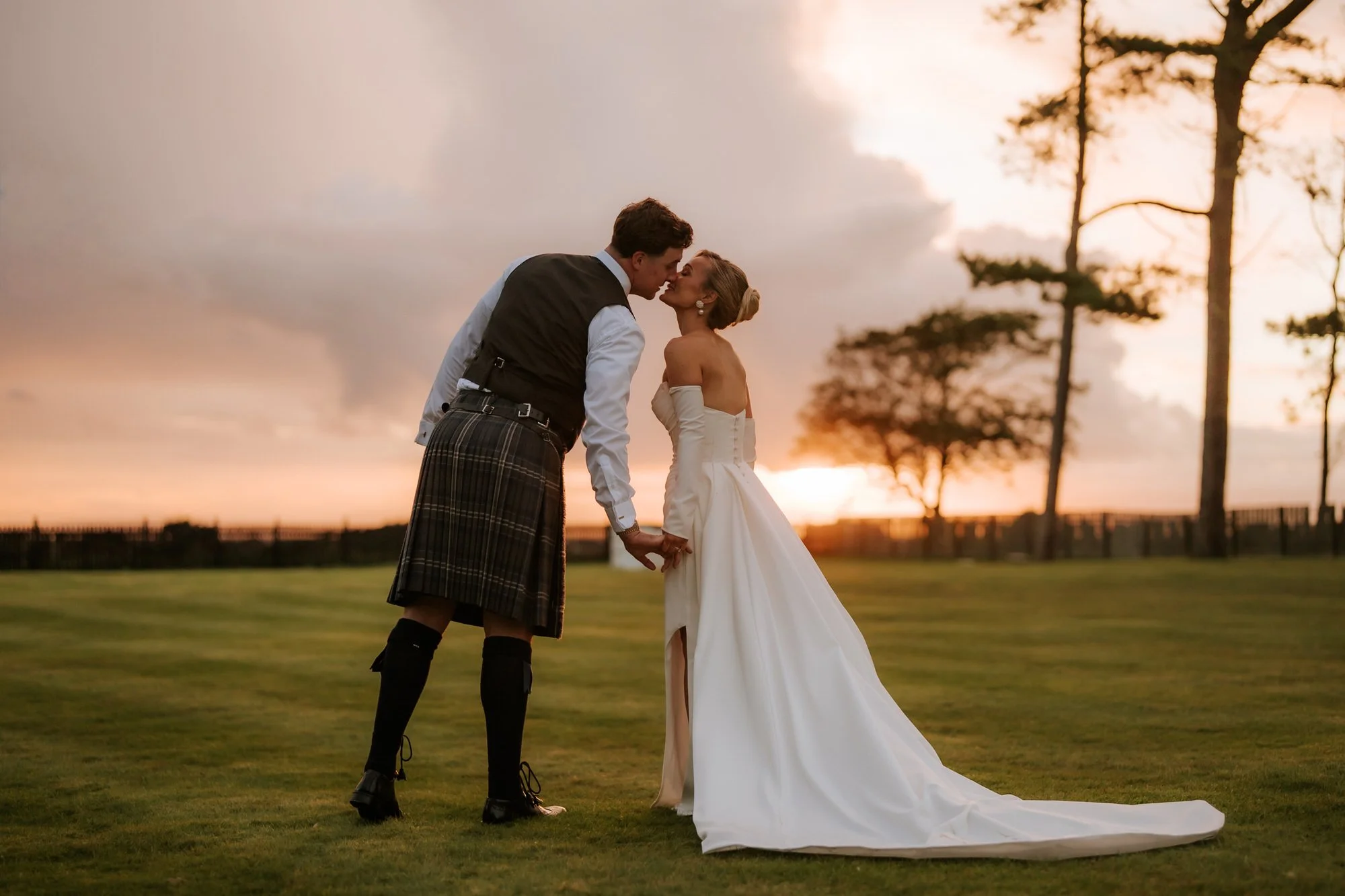 Fiona and Connor kissing on the lawn in warm evening light.