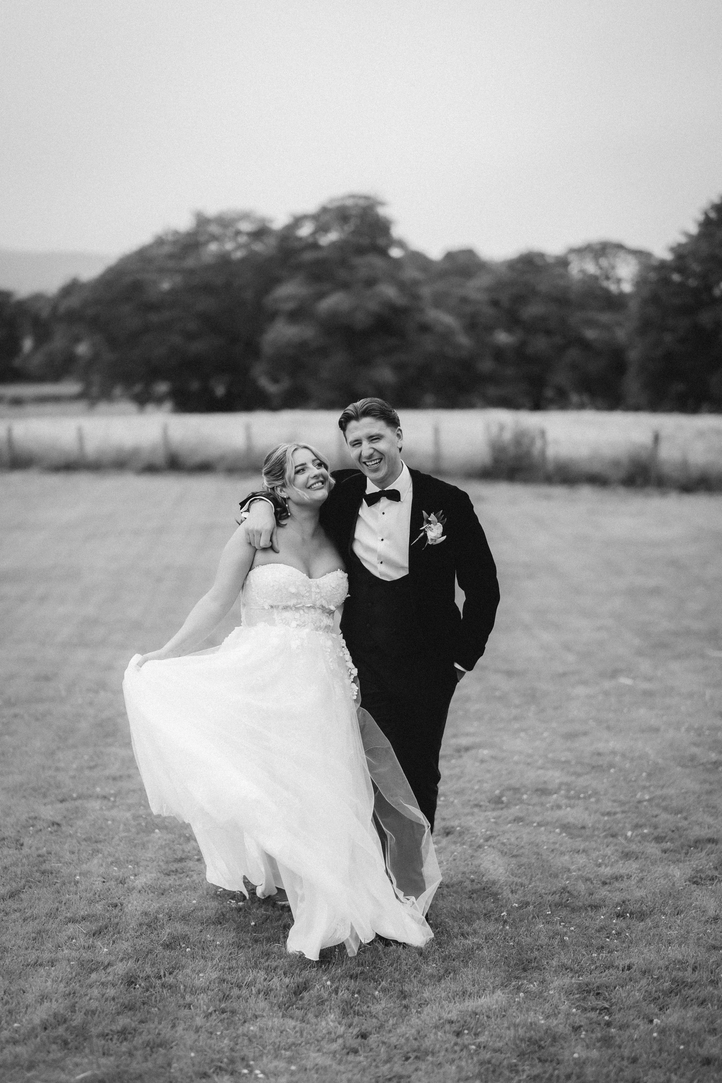 Emma and Frazer walking across the grounds in a relaxed black-and-white wedding portrait.