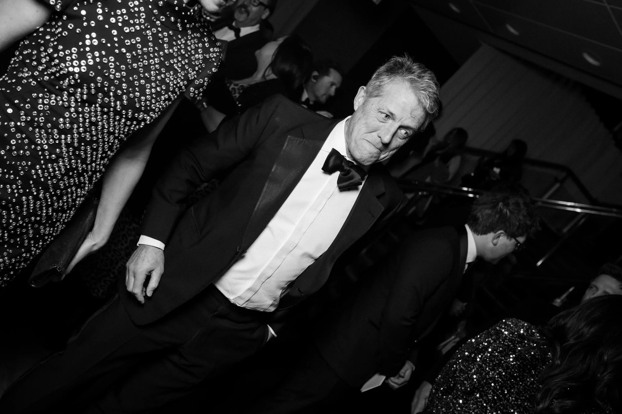 A candid black-and-white portrait of a guest in a tuxedo beside the stairs at the BAFTAs.