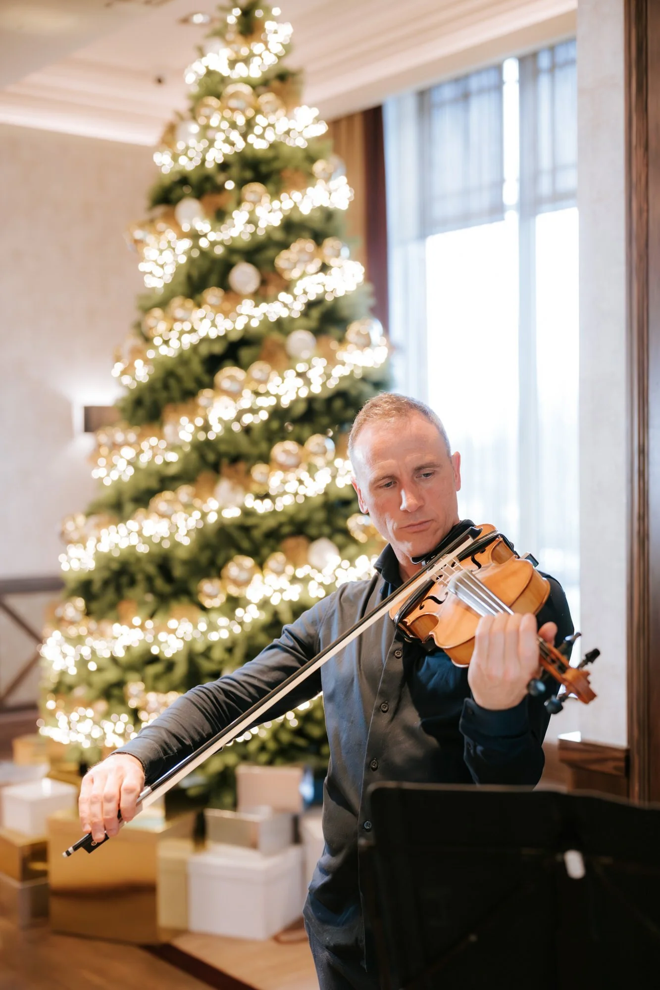 Violinist performing beside a glowing Christmas tree