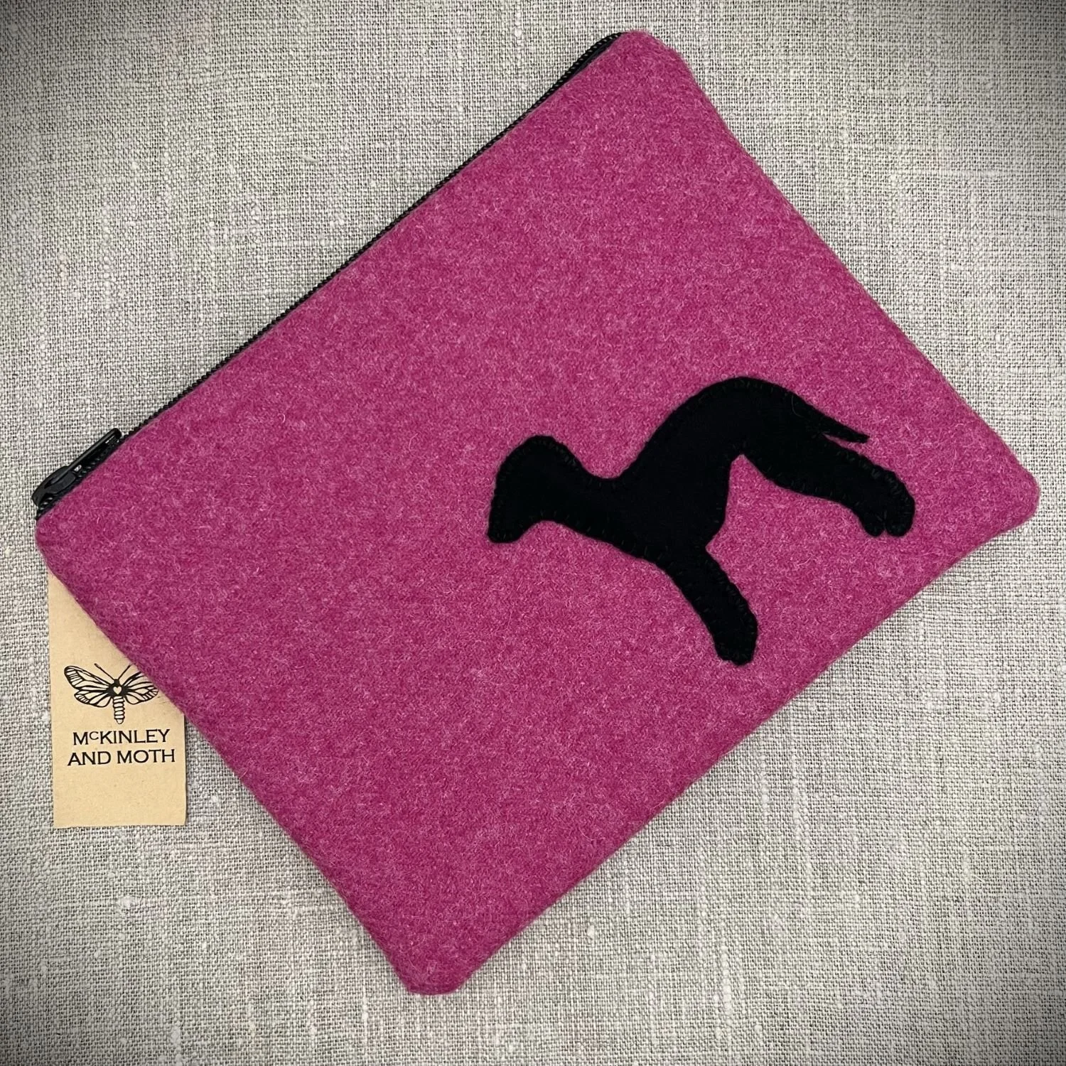 A bright pink zipped bag with a black Bedlington Terrier silhouette stitched on the front.