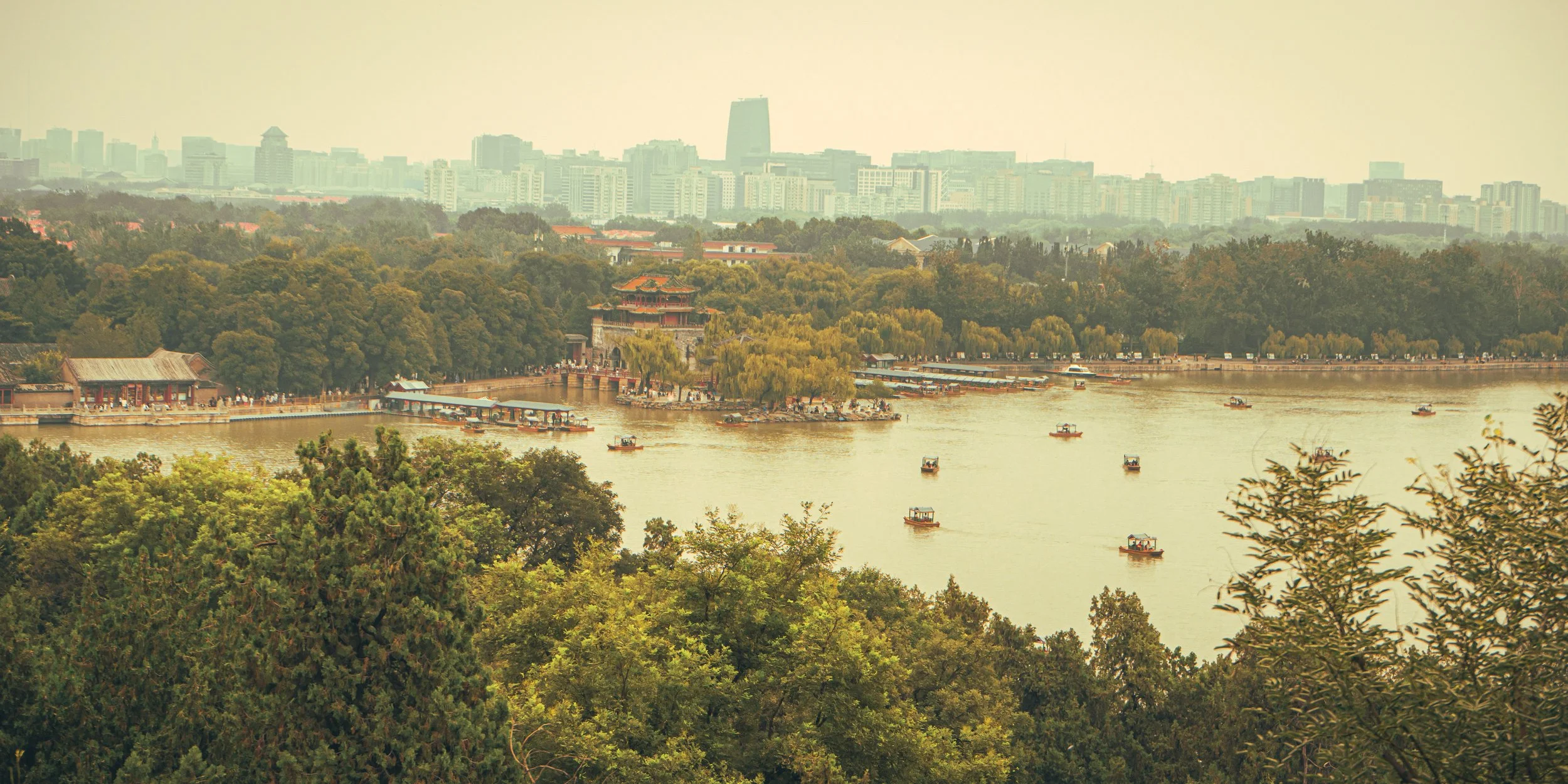 A scenic view of a river with boats, surrounded by lush greenery and traditional Chinese architecture, with a modern city skyline in the background.