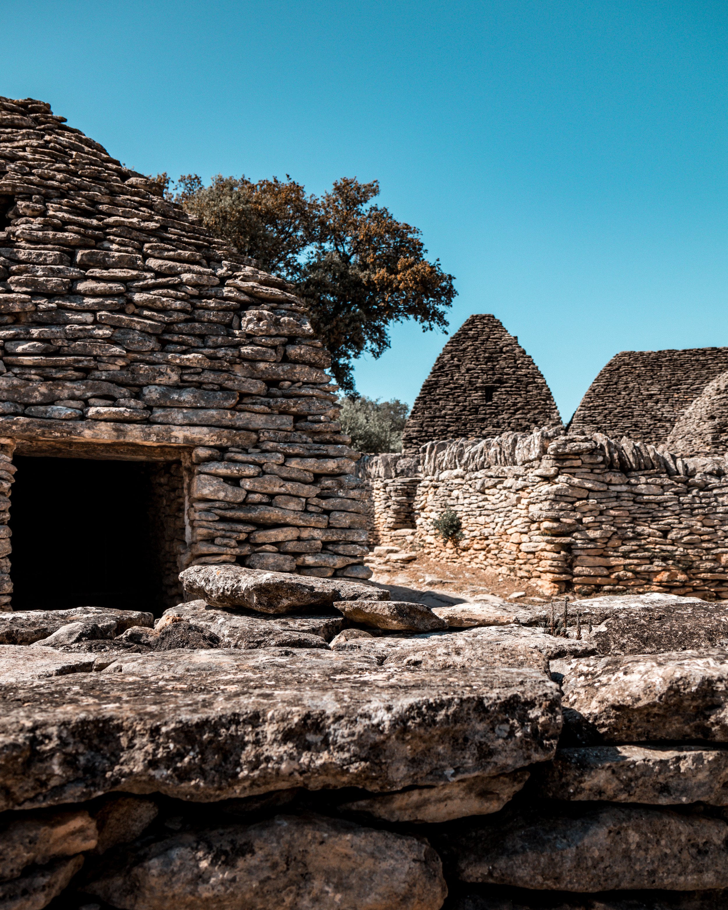Ancient stone structures with conical roofs, typical of traditional dry stone architecture, under a clear blue sky.