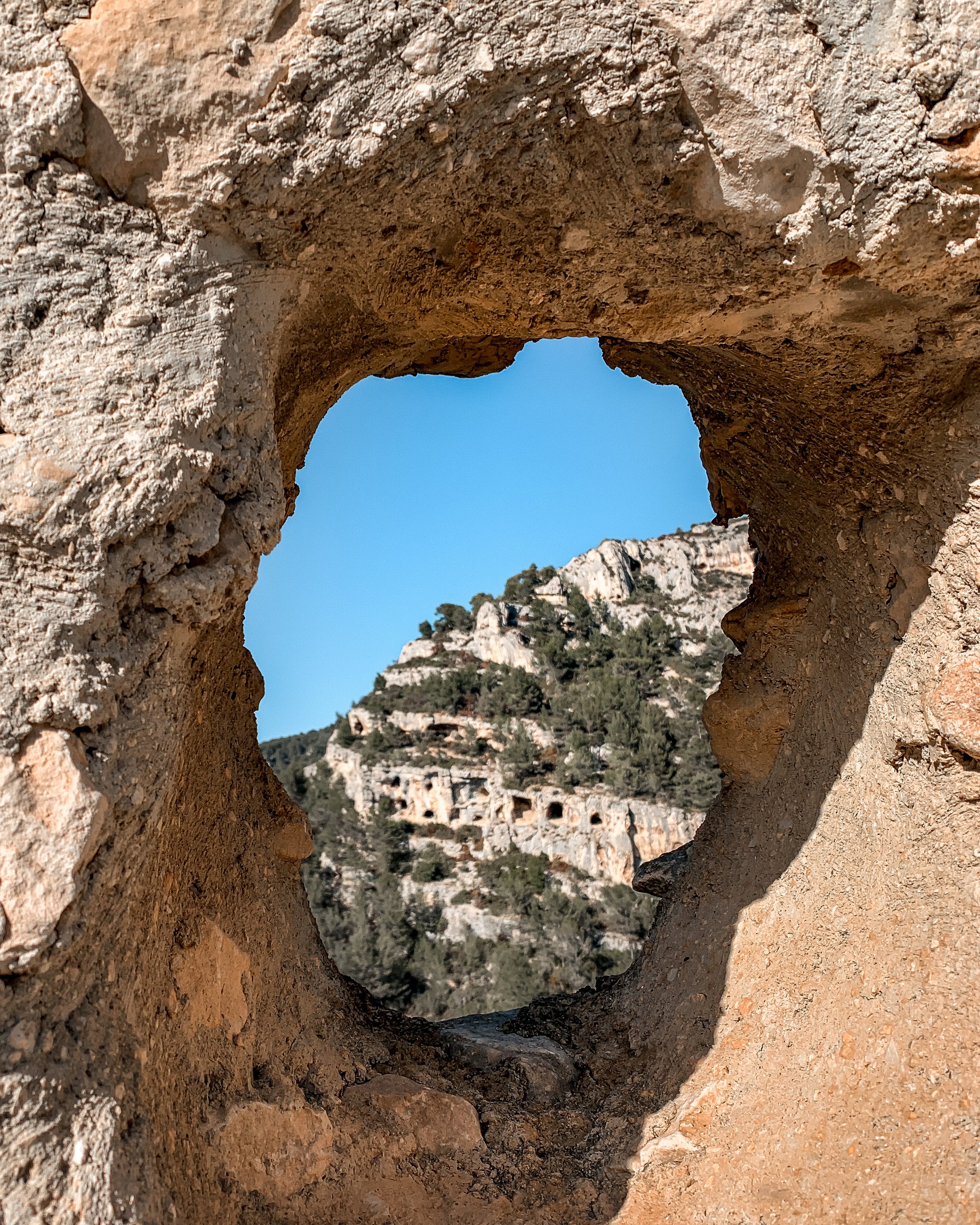 View of a mountain and ancient cave dwellings through a heart-shaped hole in a stone wall.