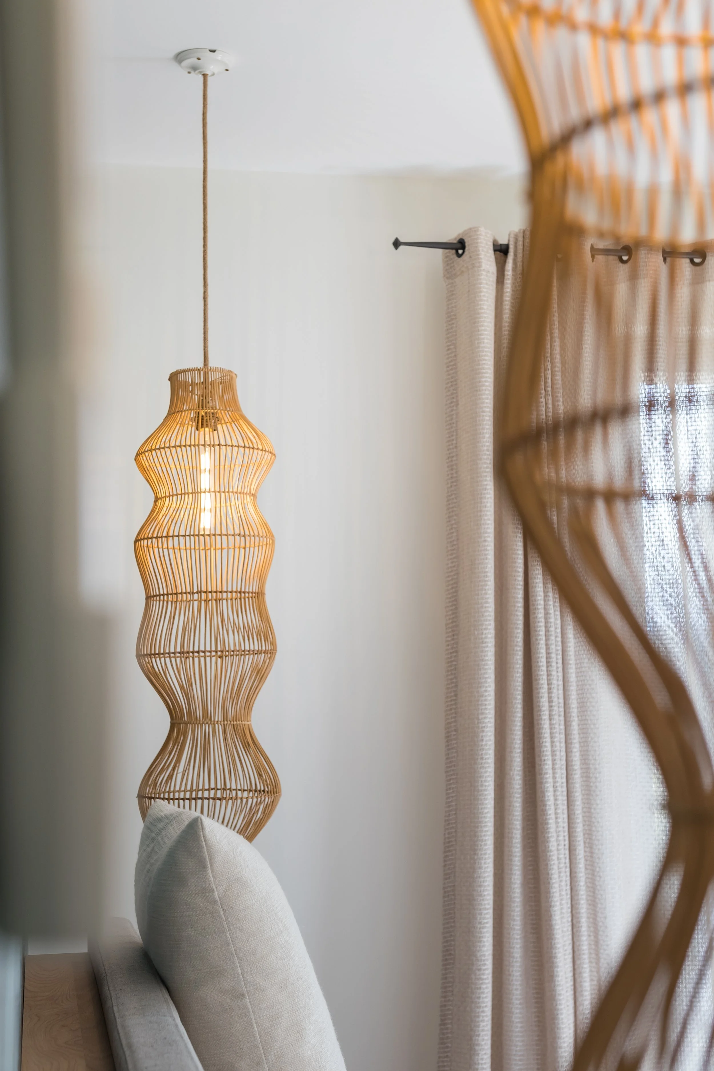 Interior view of a room with a beige headboard, a woven rattan pendant light, and cream-colored curtains.