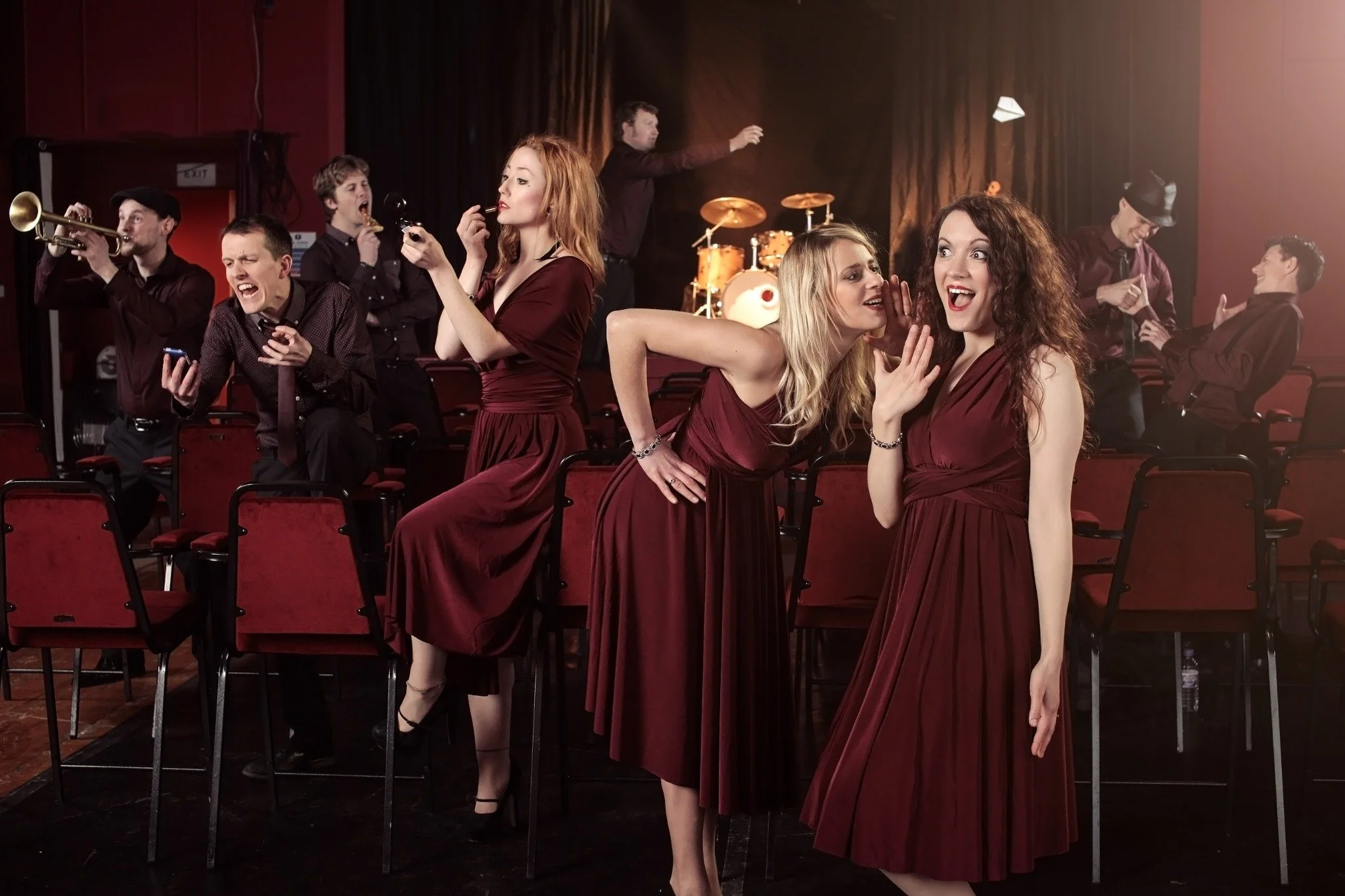 Hot Jazz Biscuits musicians and singers in maroon stage outfits, laughing together on stage.