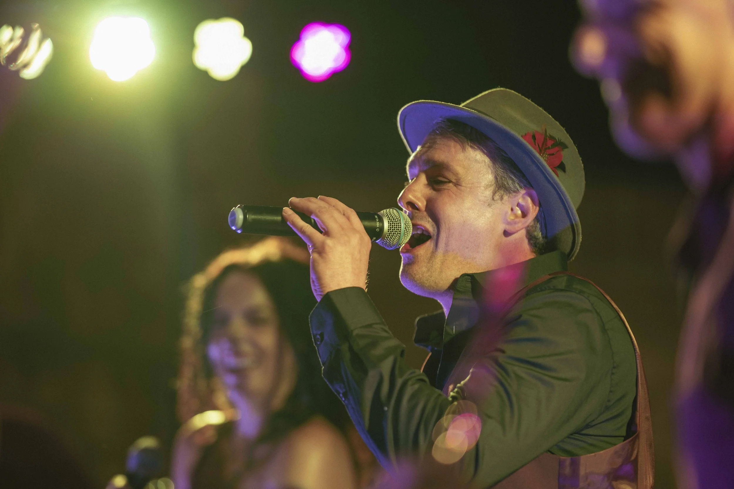 Hot Jazz Biscuits vocalist singing into a handheld microphone beneath colourful stage lights.