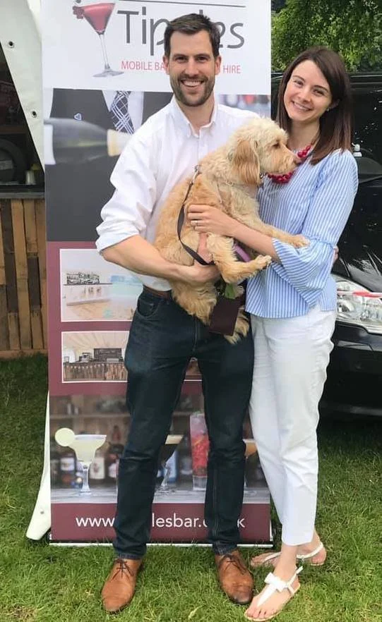 Tim and Charlotte of Tipples smiling with their dog in front of Tipples branding.