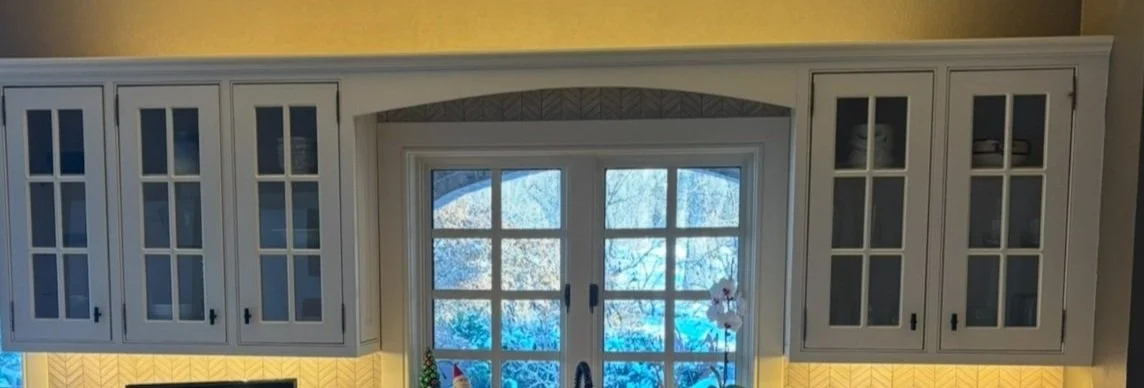 Kitchen with white cabinets, decorative window over the sink, and yellow patterned backsplash.
