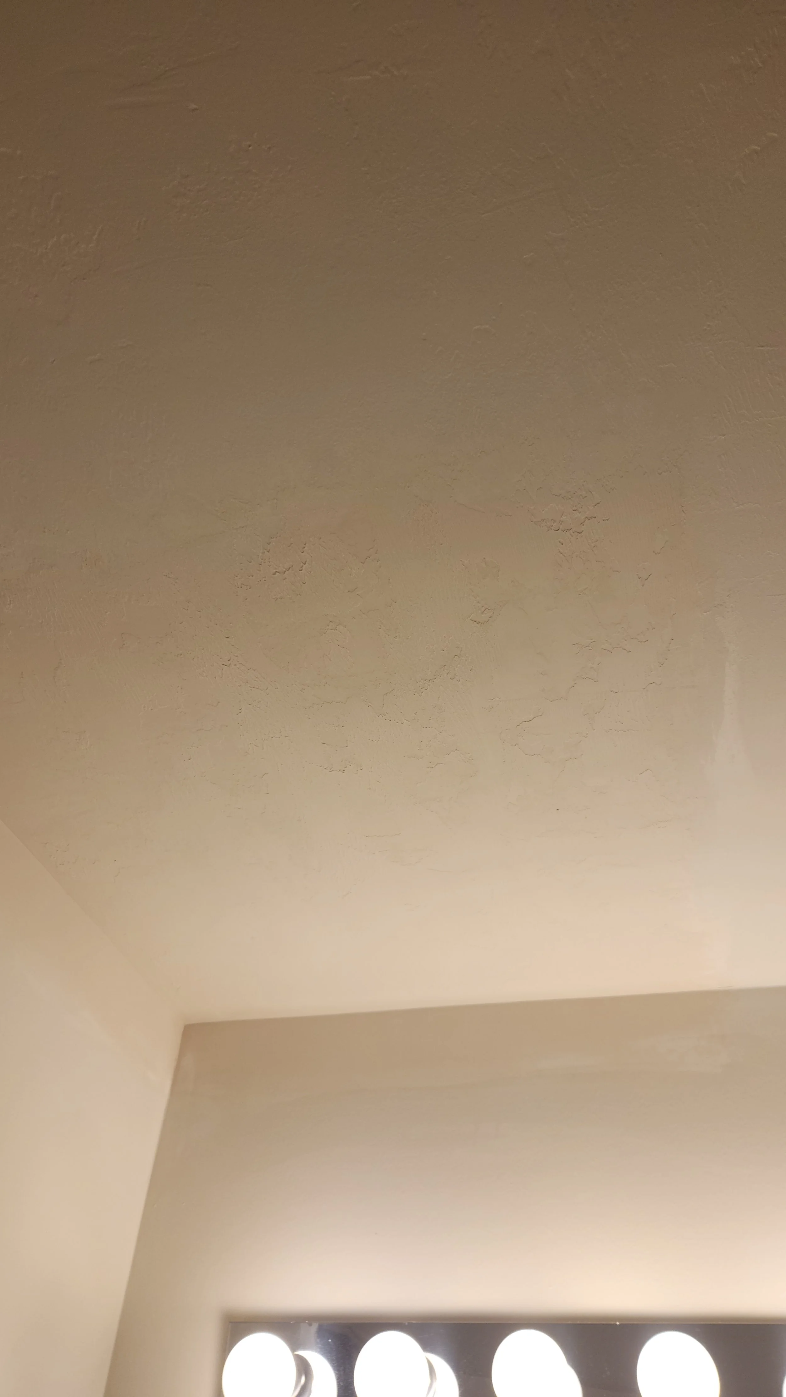 Ceiling with textured paint and a partial view of a light fixture with bulbs at the bottom of the image.