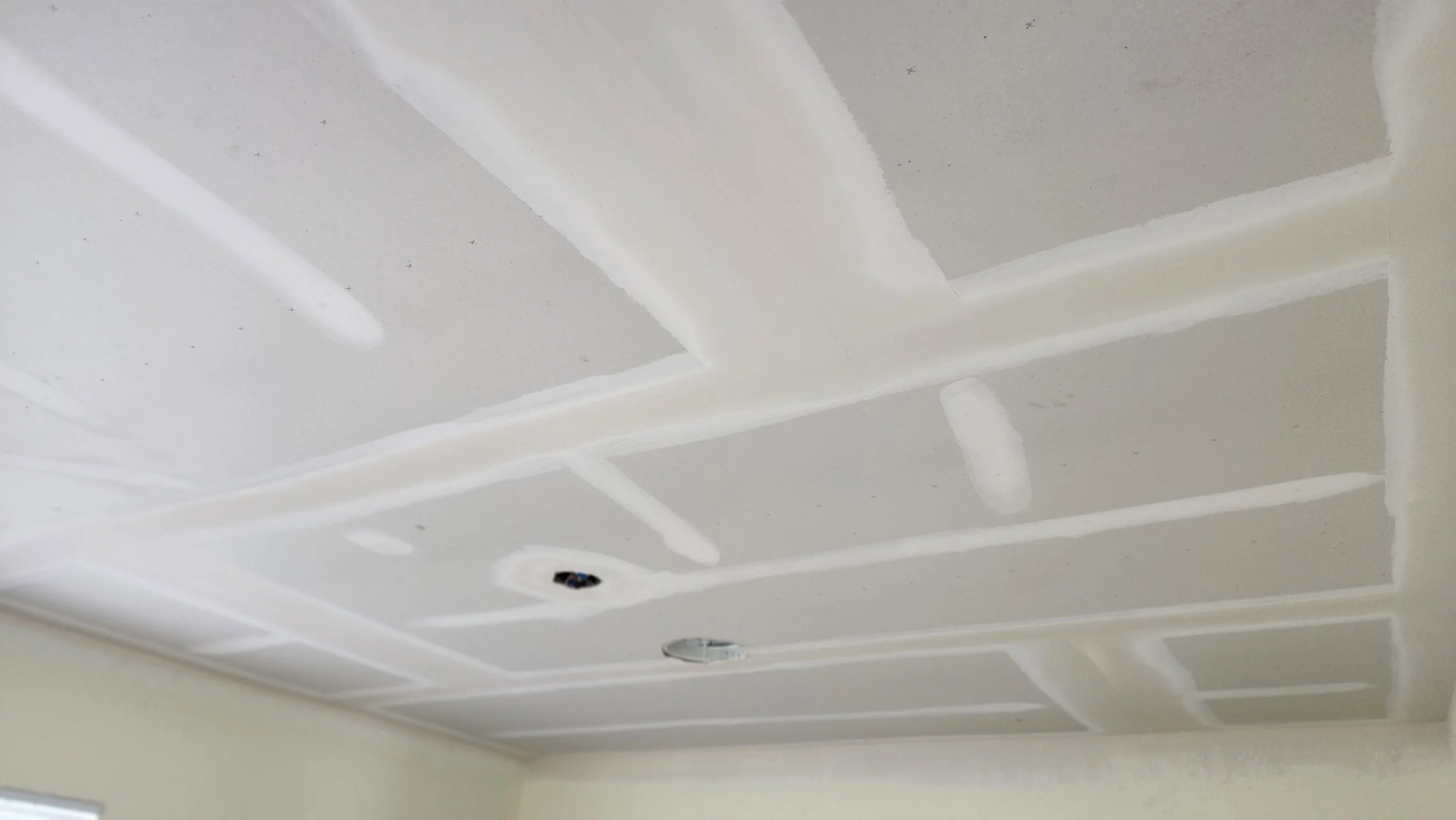 Ceiling with drywall panels and joint compound applied to seams, with two light fixtures not yet installed.